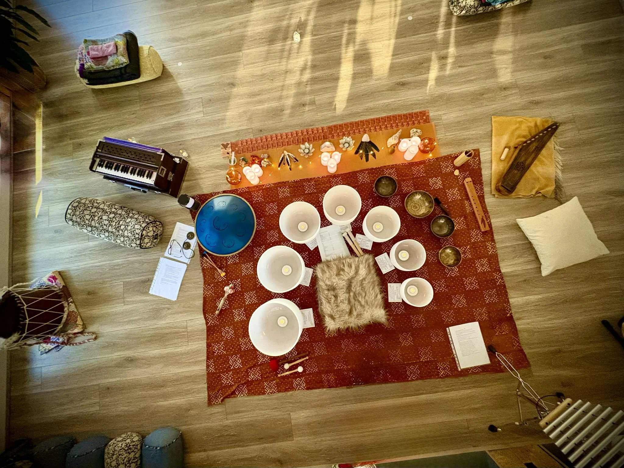 A top-down view of a space decorated with candles and spiritual items on a red cloth, with various musical instruments and objects nearby, on a wooden floor.