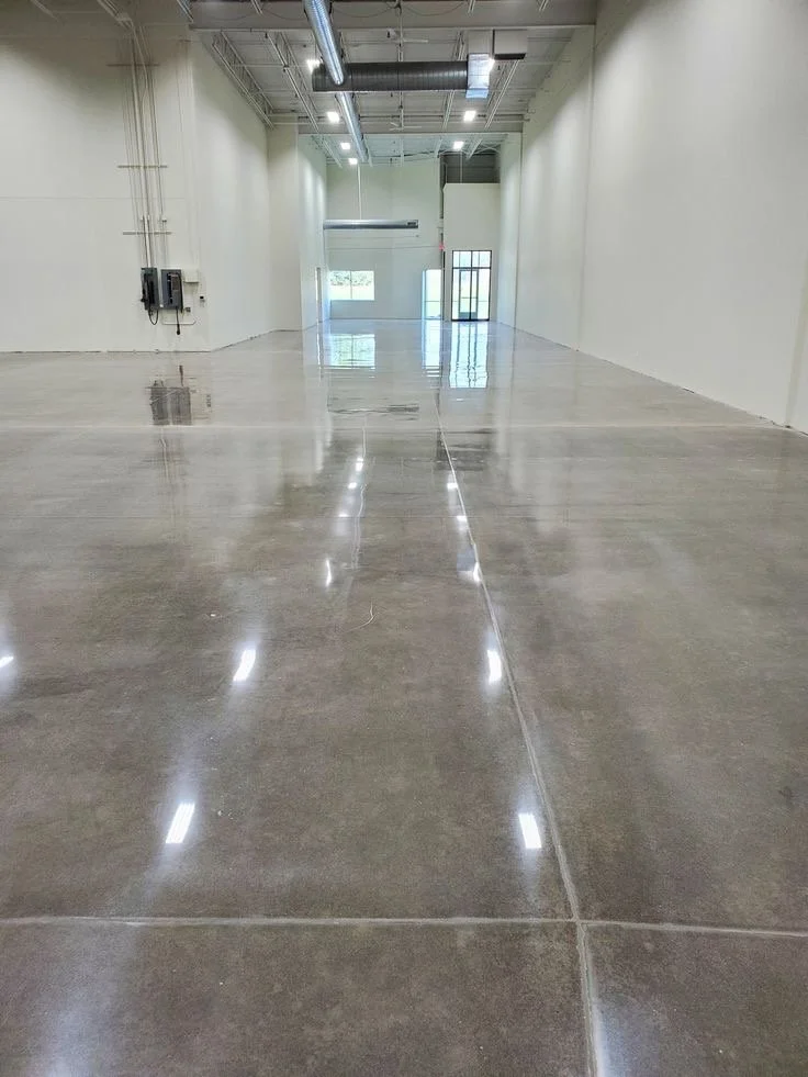 Empty commercial space with polished concrete floors, white walls, high ceilings, and industrial lighting fixtures.