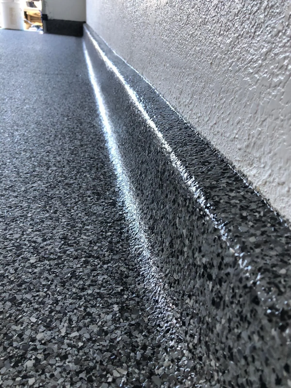 Close-up of a textured black and gray speckled epoxy floor surface and a raised black threshold at the base of a wall.