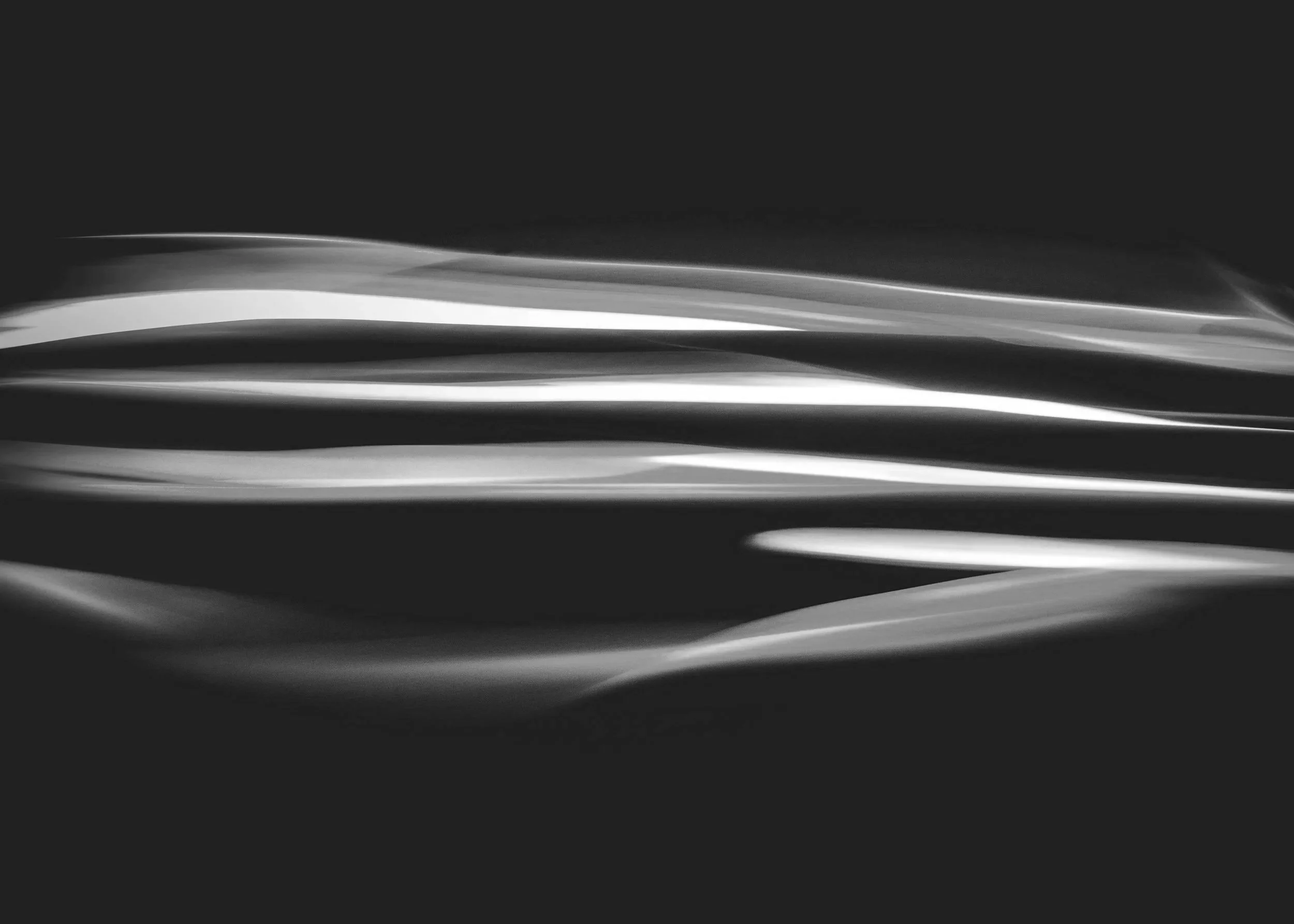 Black and white abstract image with smooth flowing light streaks across a dark background.