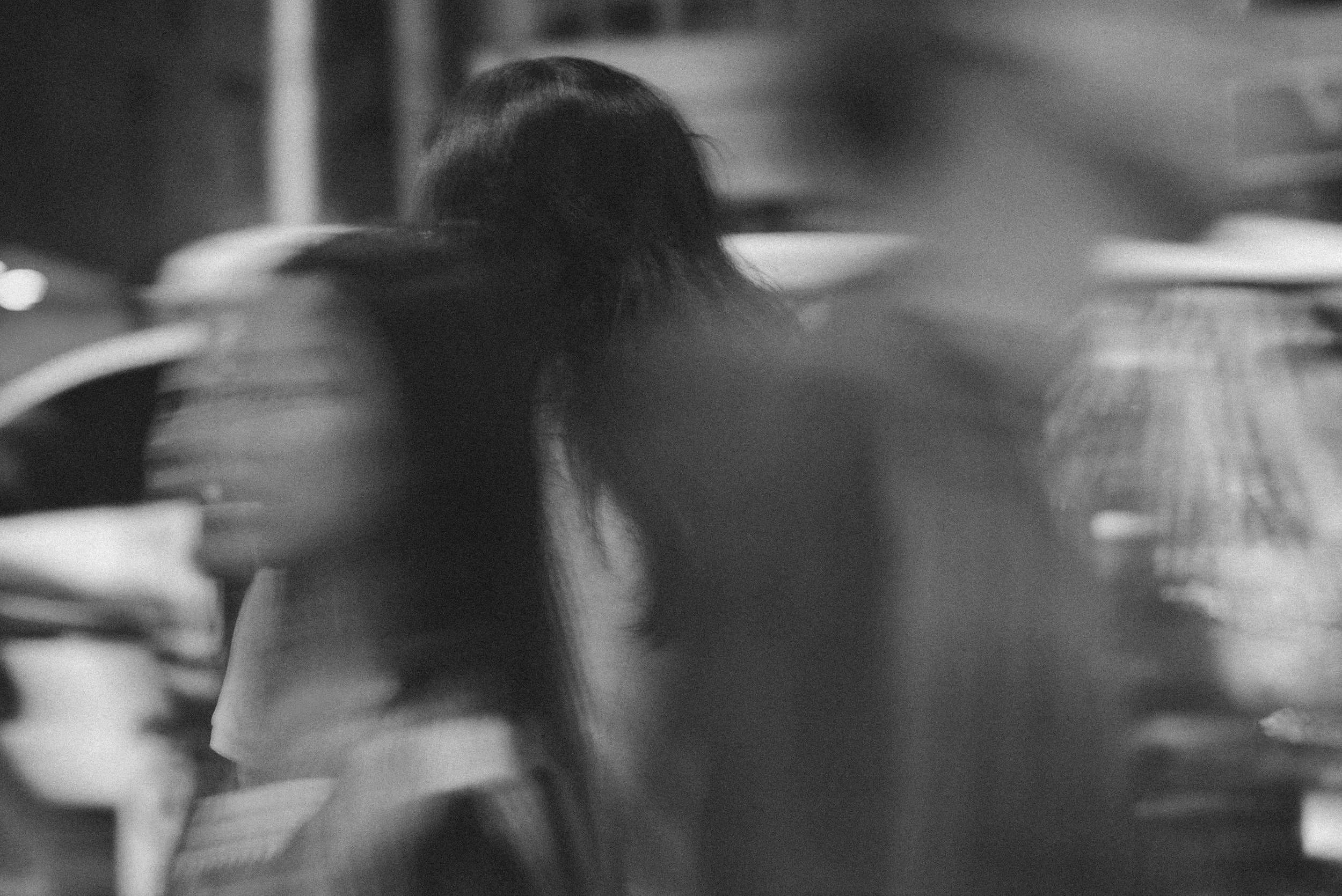 A close-up black-and-white photograph of a person's face, partially obscured, with background and surroundings out of focus.