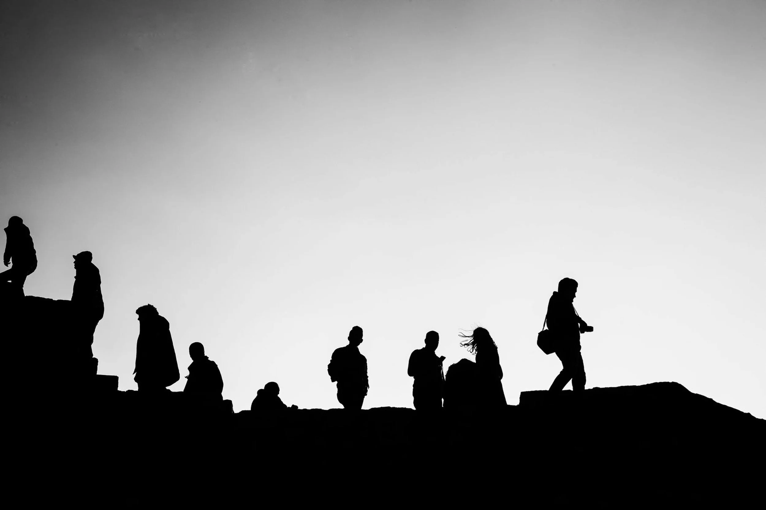 Silhouettes of people walking and sitting on a ledge against a clear sky