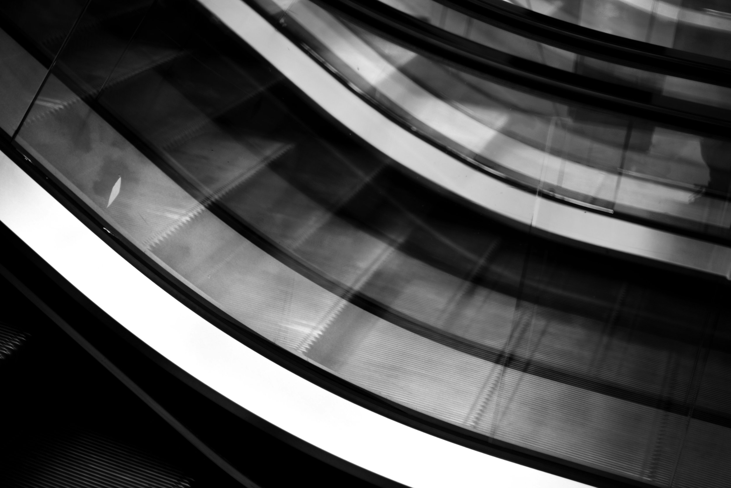 Close-up of an escalator with metallic steps and glass sides, captured in black and white.