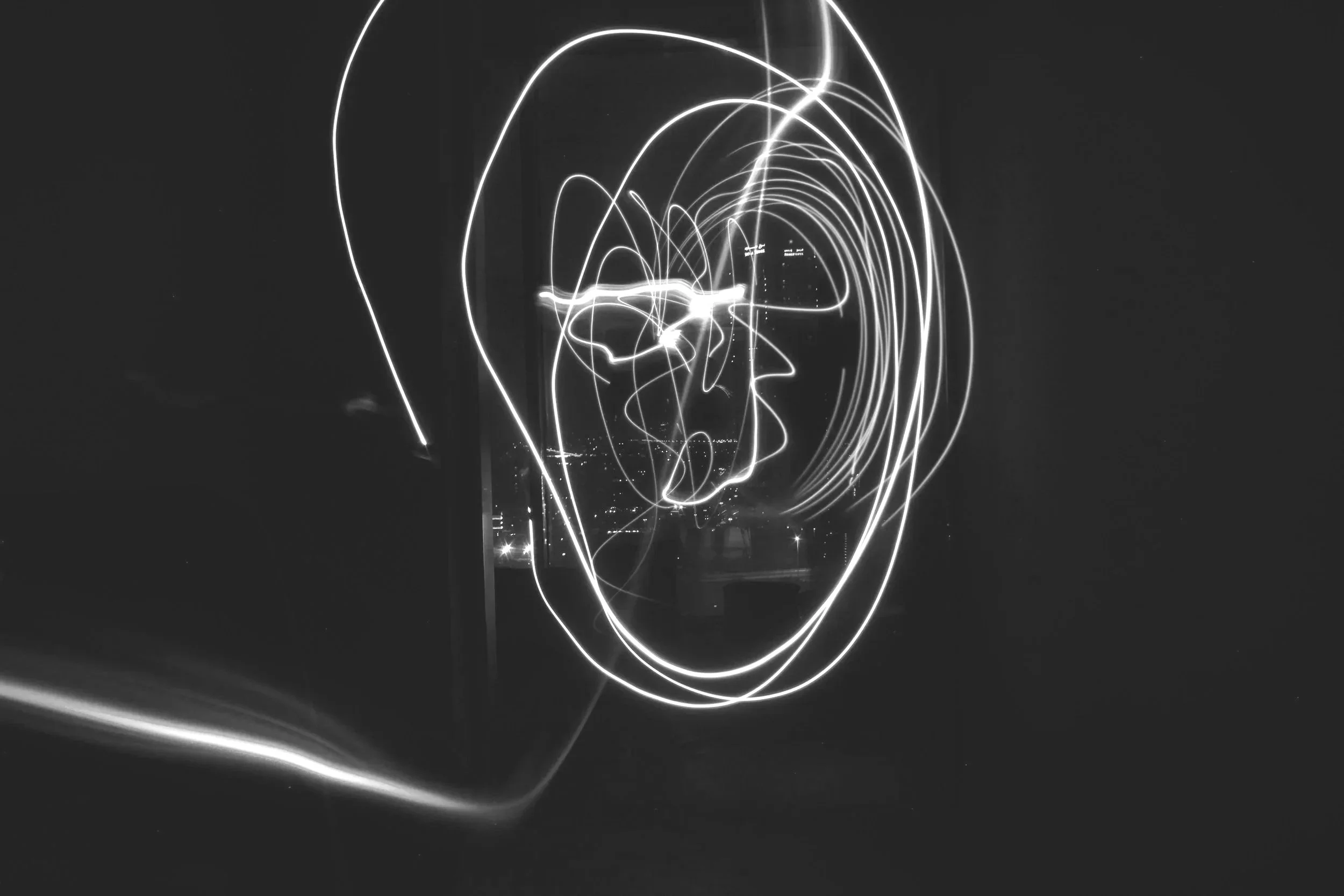 Black and white abstract image of light trails forming a face outline with glasses and hair, set against a dark background.