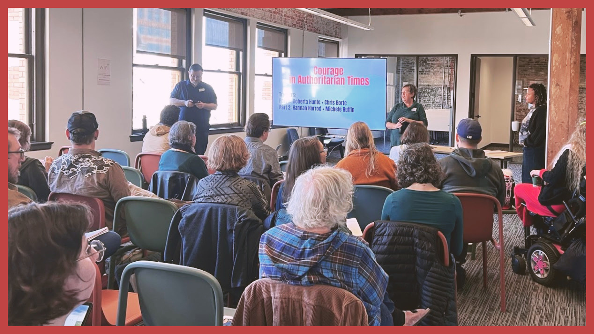 A group of people attending a presentation in a bright room with large windows. The presenter stands next to a large screen that reads 'Courage in Authoritarian Times'.