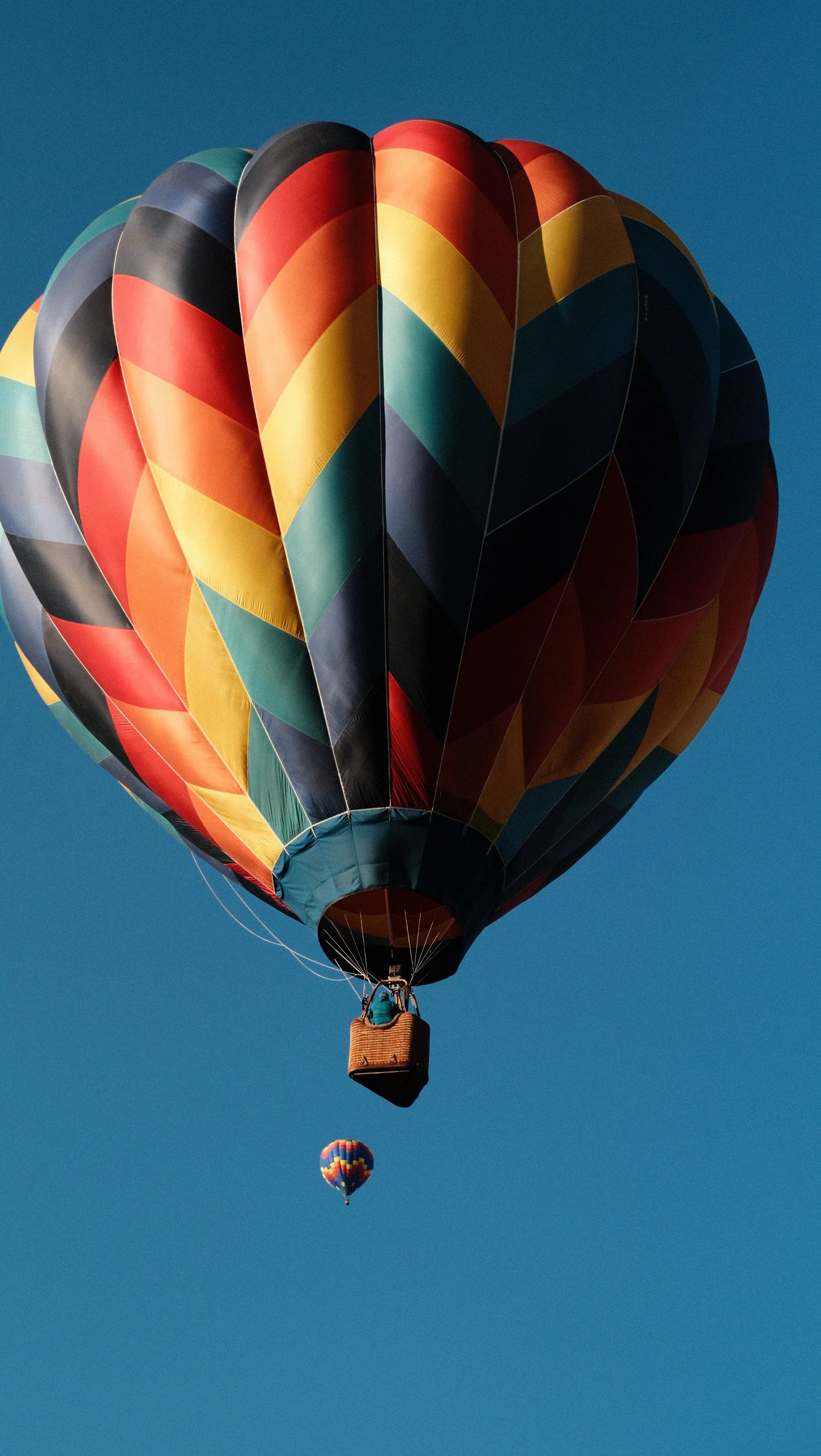 Two hot air balloons floating in the sky, one larger with a colorful pattern and a smaller in the background.