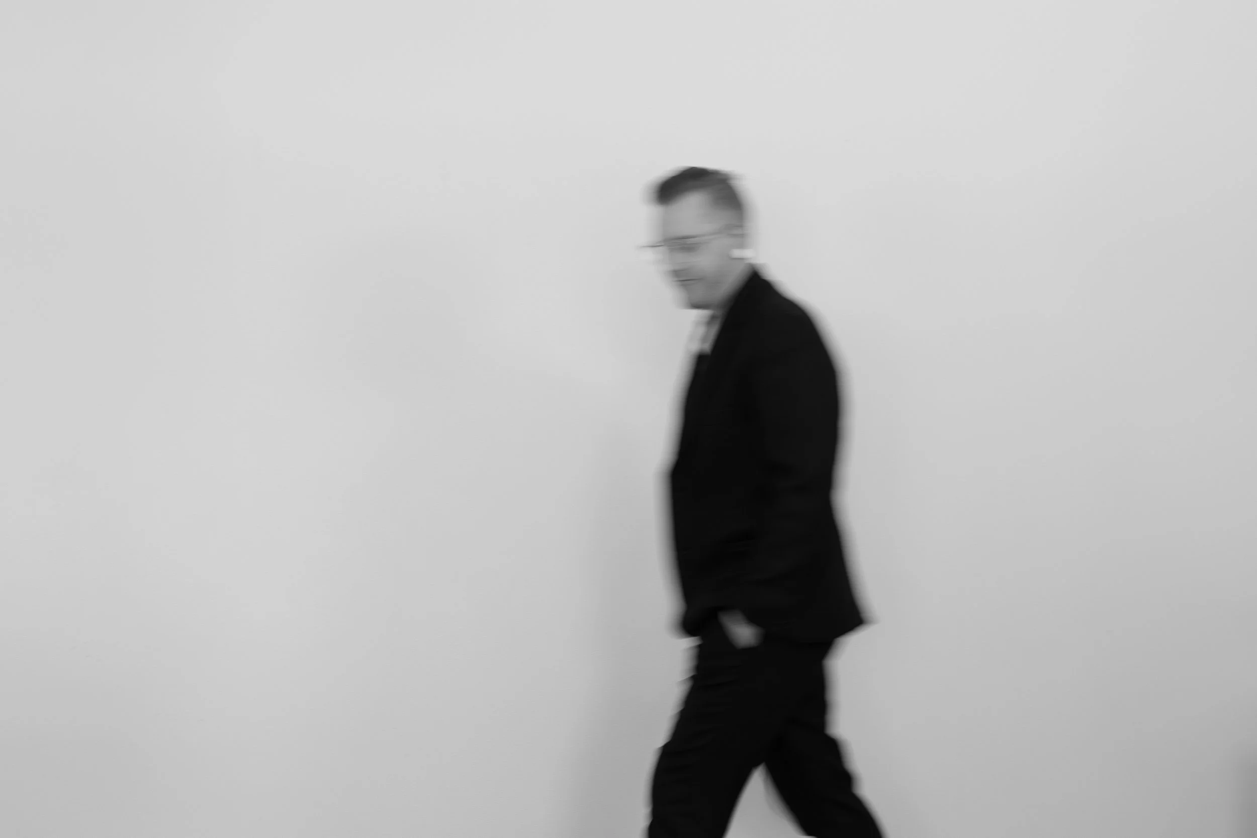 A blurred black and white photo of a person walking in profile with a blank background.