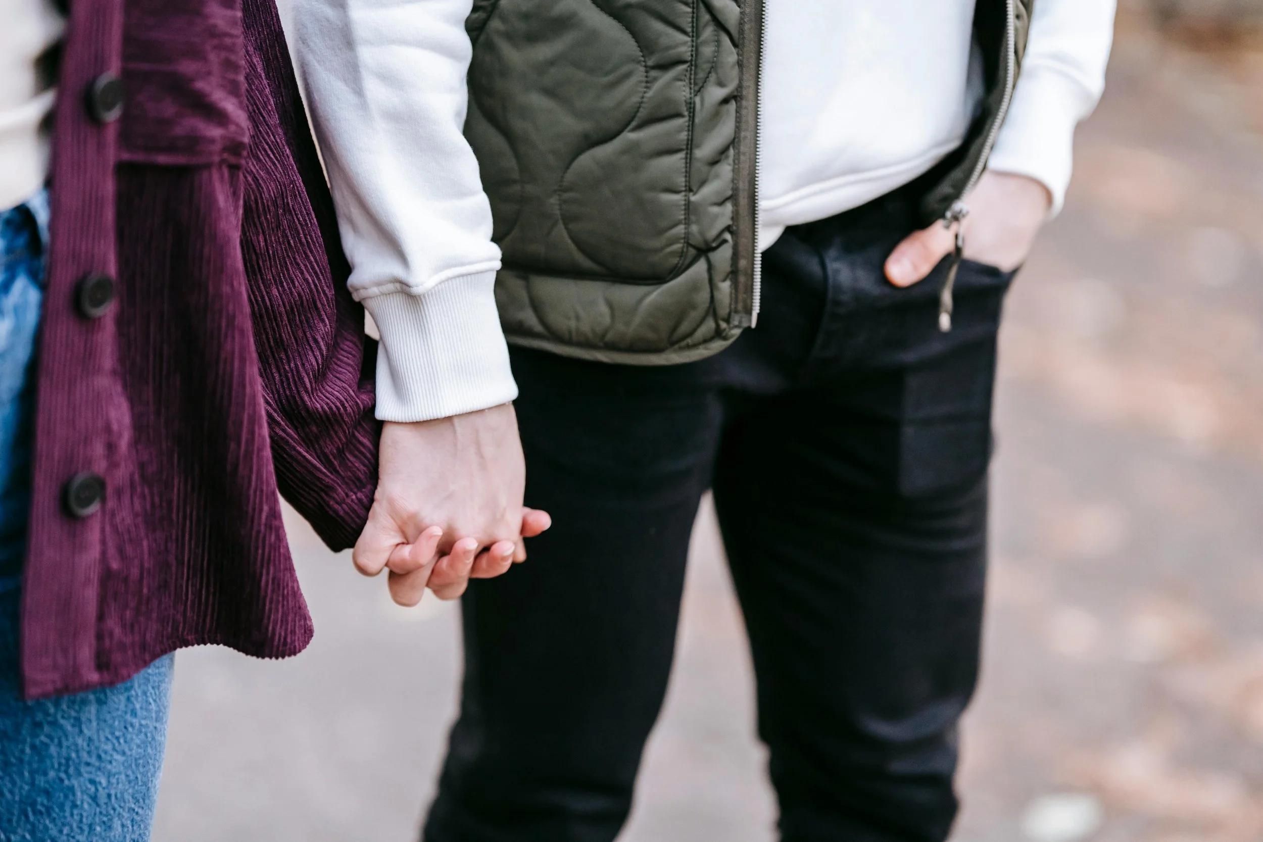 Close-up of two people holding hands, standing side by side outdoors.