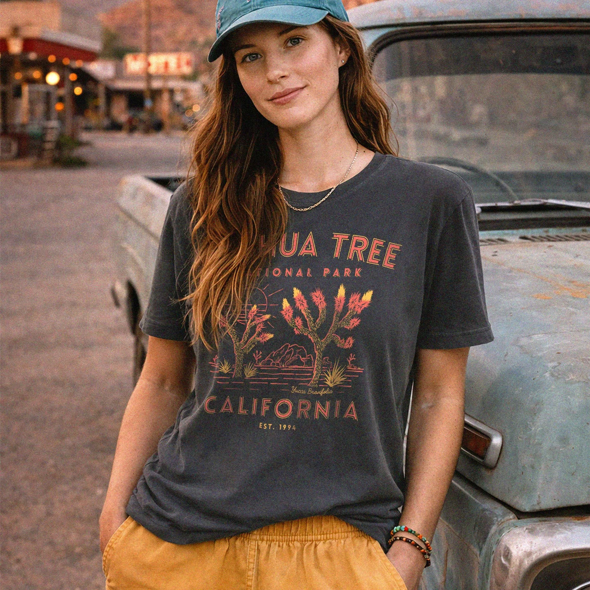 a woman wearing a joshua tree national park tee while posing next to an old truck