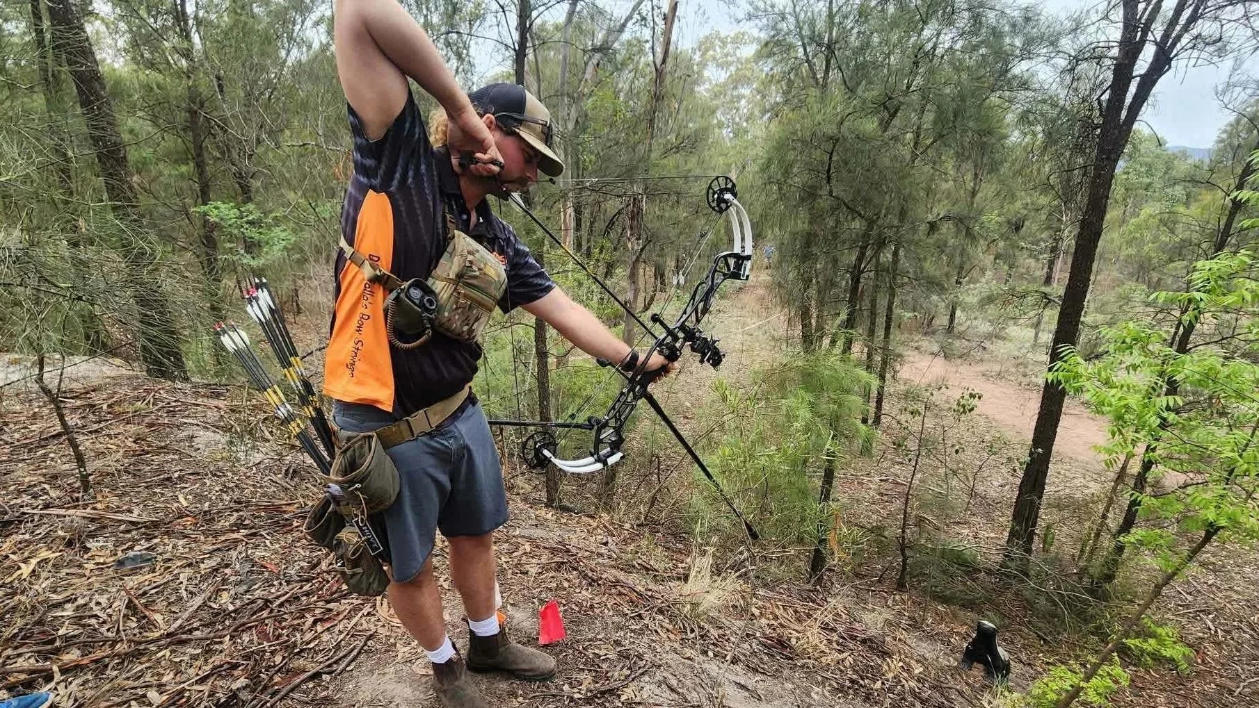 A man with a bow, quiver, and camouflage gear in a wooded area