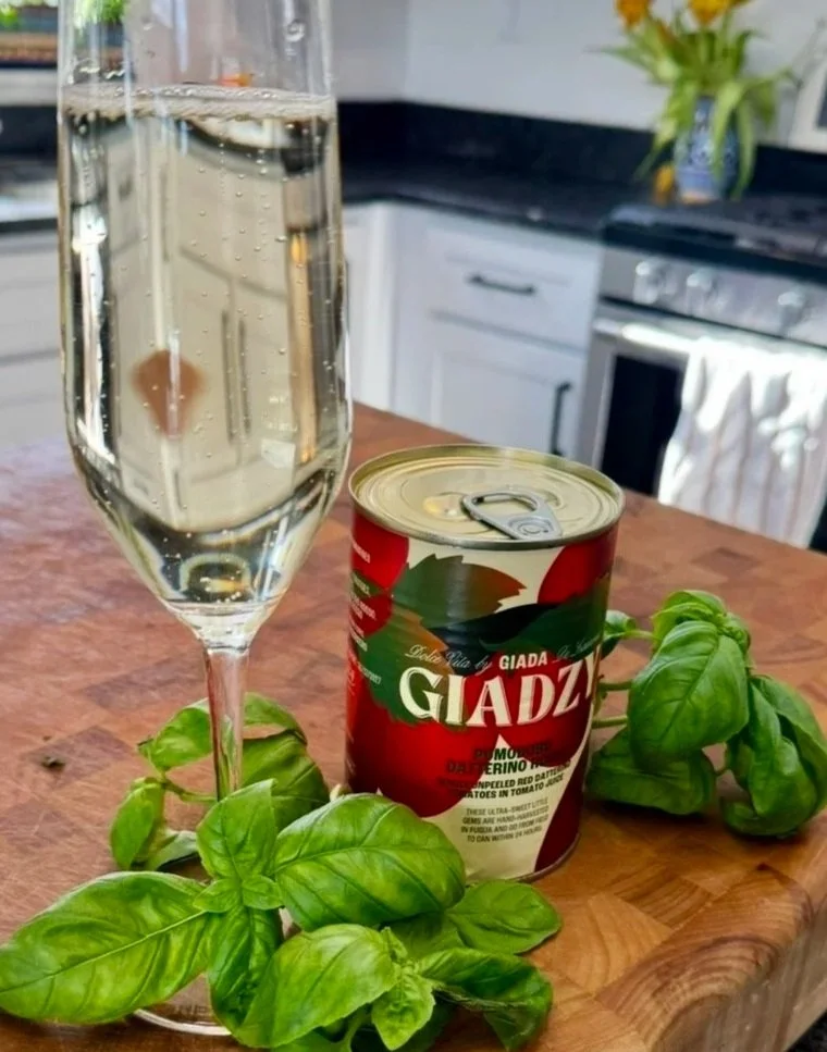Giadzy Pomodorino di Corbara tomatoes with a glass of prosecco and fresh basil on a wood butcher block — ingredients for a no-cook wood fired pizza sauce