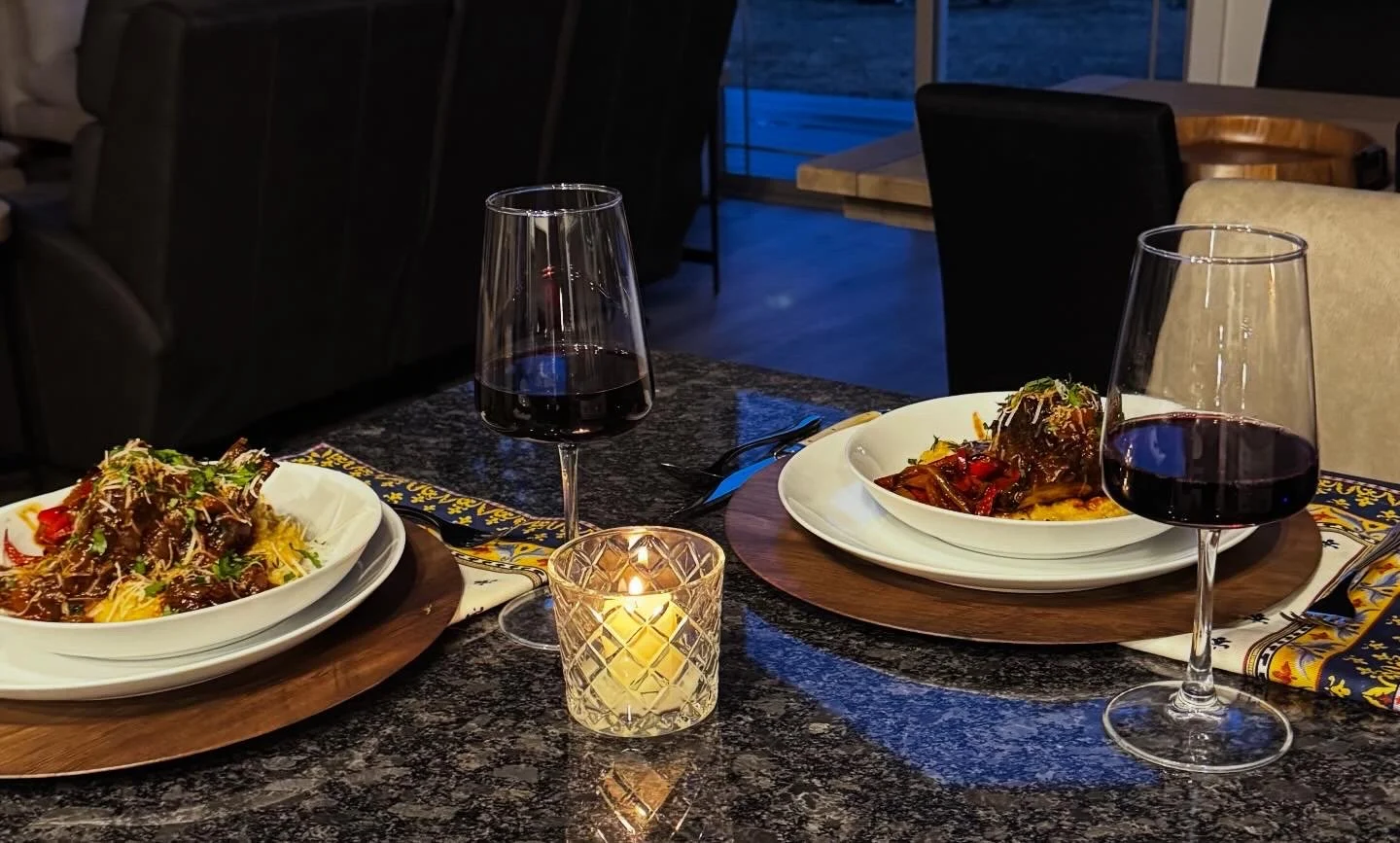 Braised short ribs served over creamy polenta with red wine and candlelight on a set dinner table