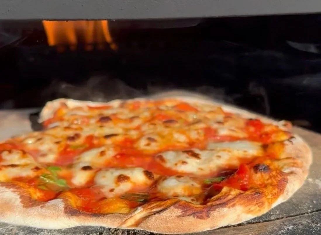 Wood fired pizza cooking inside a Solo Stove Pi pizza oven with orange flames glowing and steam rising from the crust