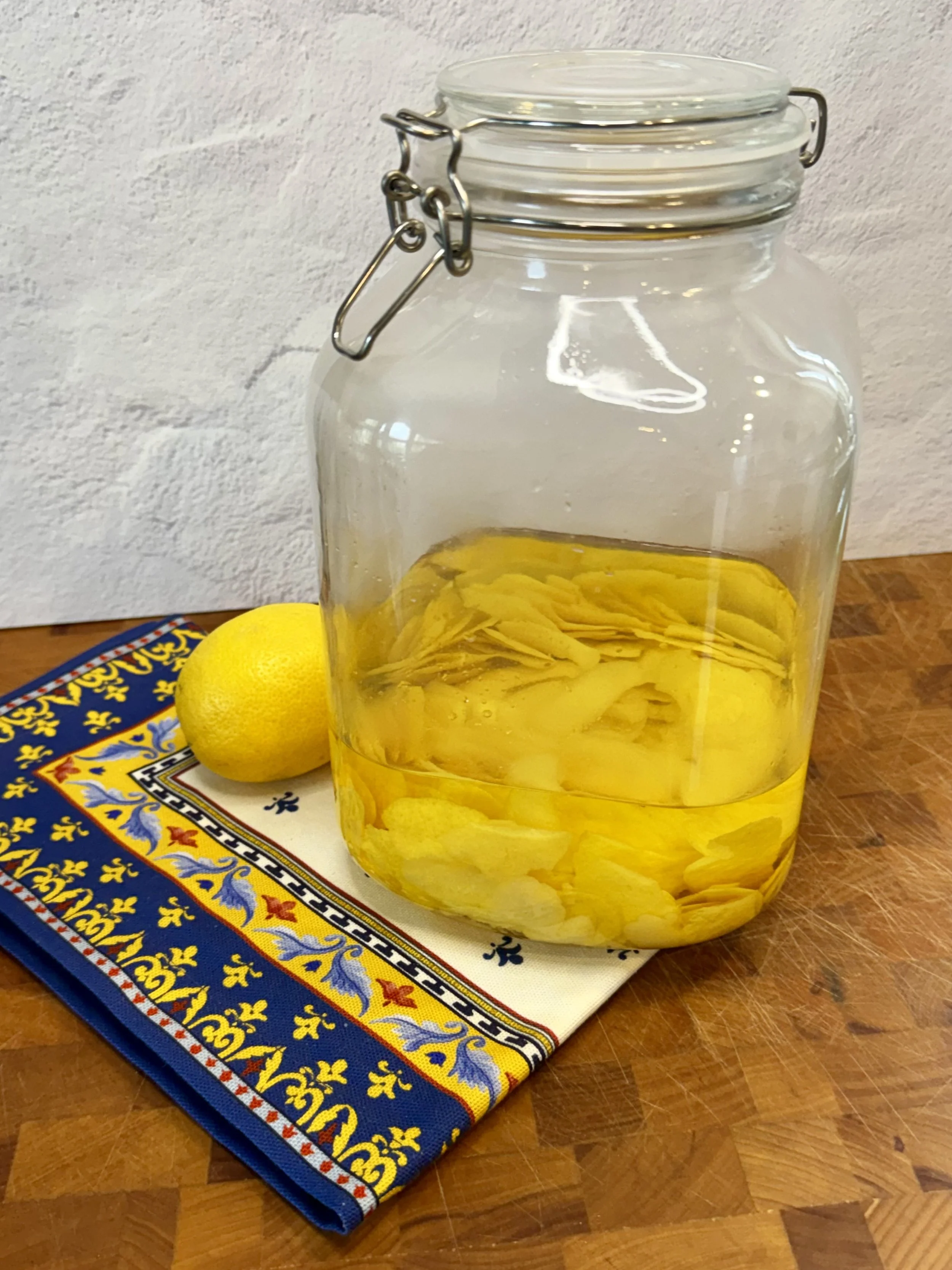Lemon peels steeping in vodka in a glass jar on the counter to make homemade limoncello.