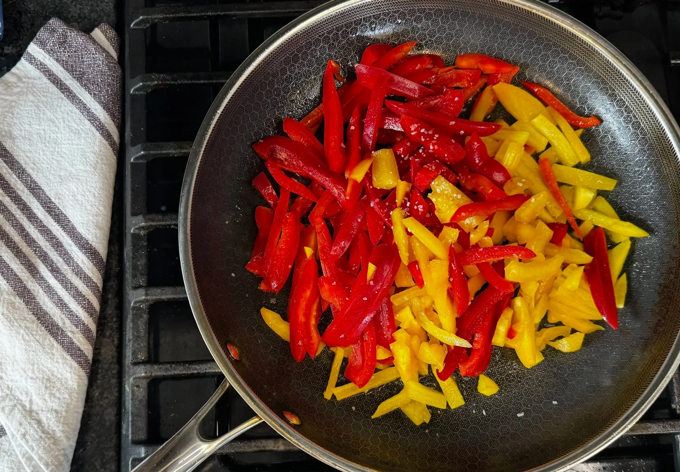 Sliced bell peppers cooking in a skillet for peperonata
