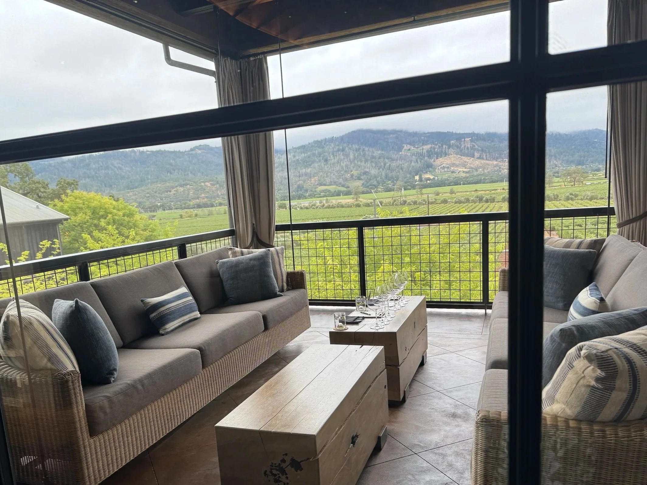 Porch with couch swings and wine glasses on table in front of vineyard