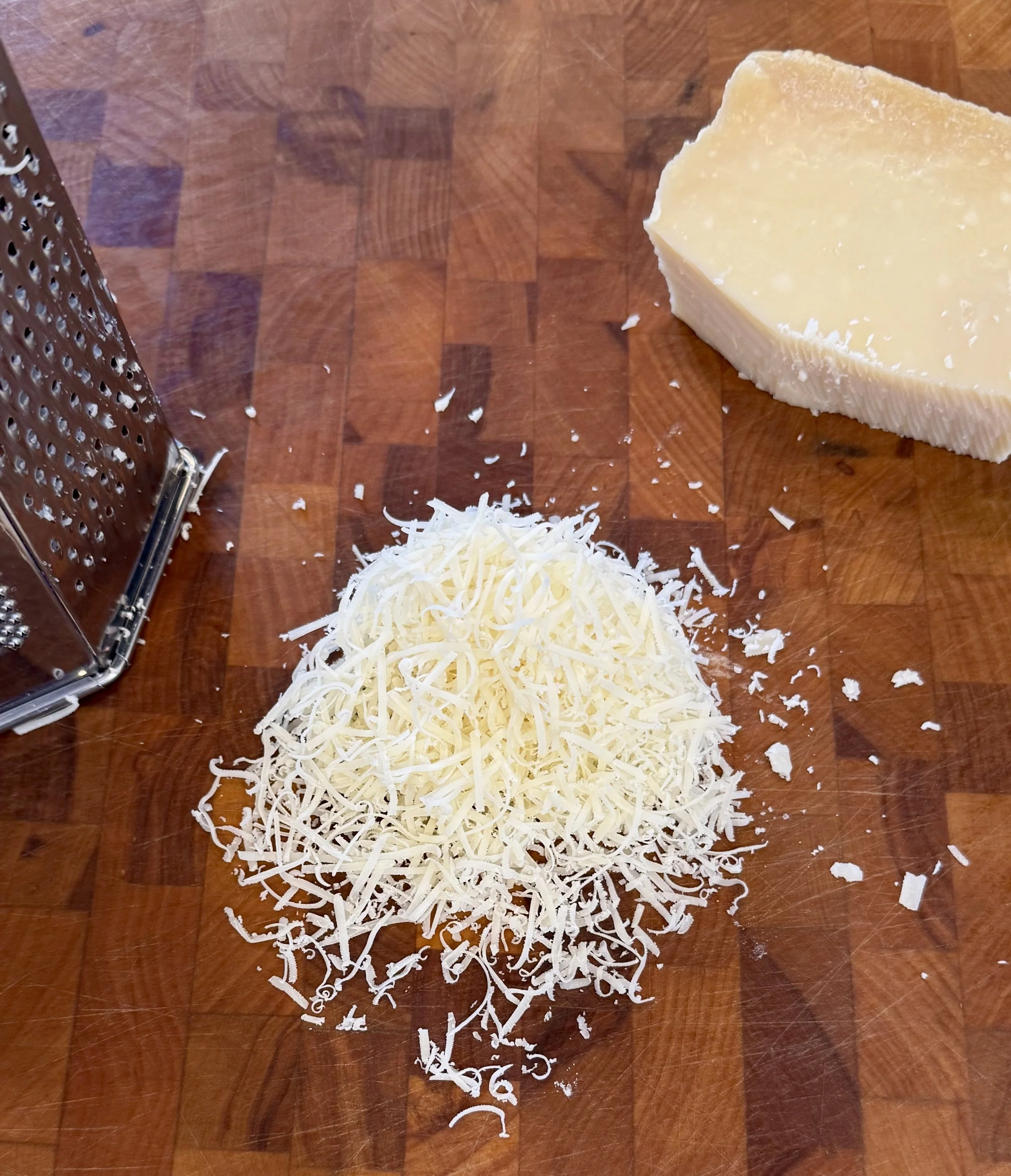 Freshly grated Parmigiano Reggiano on a wooden cutting board for red wine cream pasta