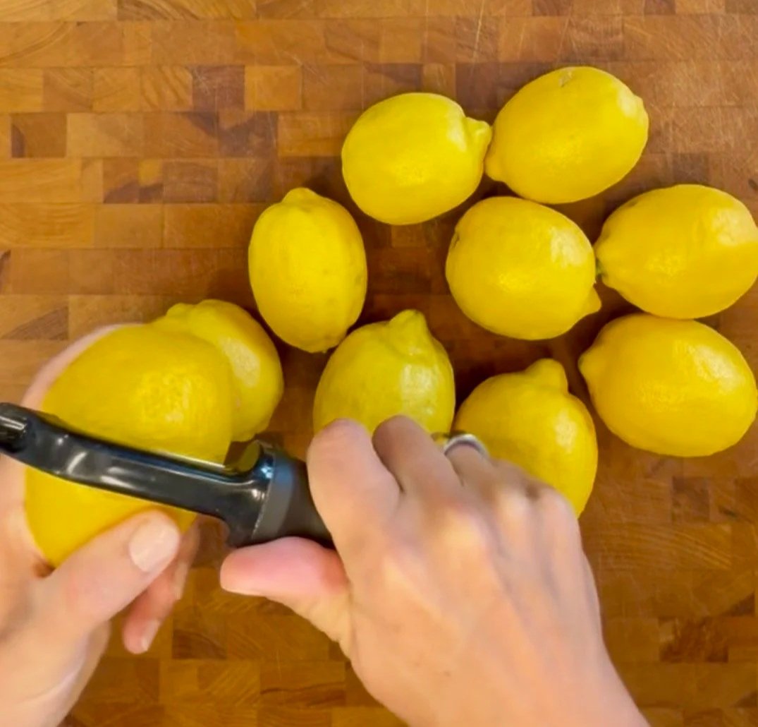 Fresh lemons on a wooden cutting board being peeled for homemade limoncello.