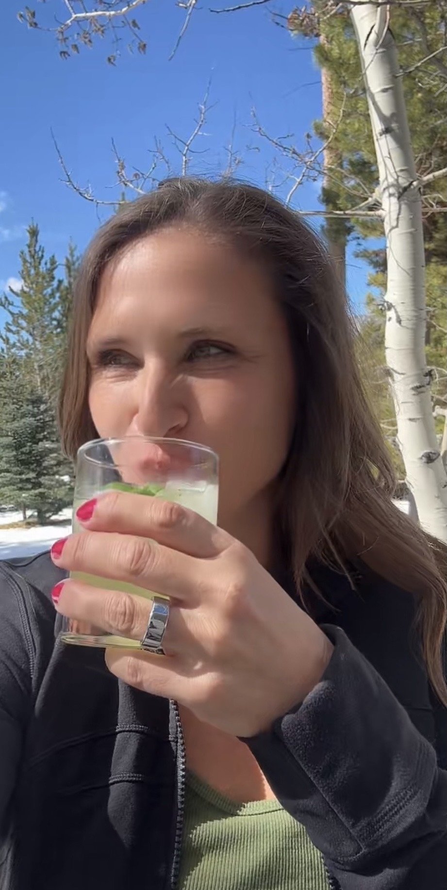 Woman drinking an Almalfi Basil Smash limoncello cocktail outdoors in the Montana mountains with snow and blue sky.