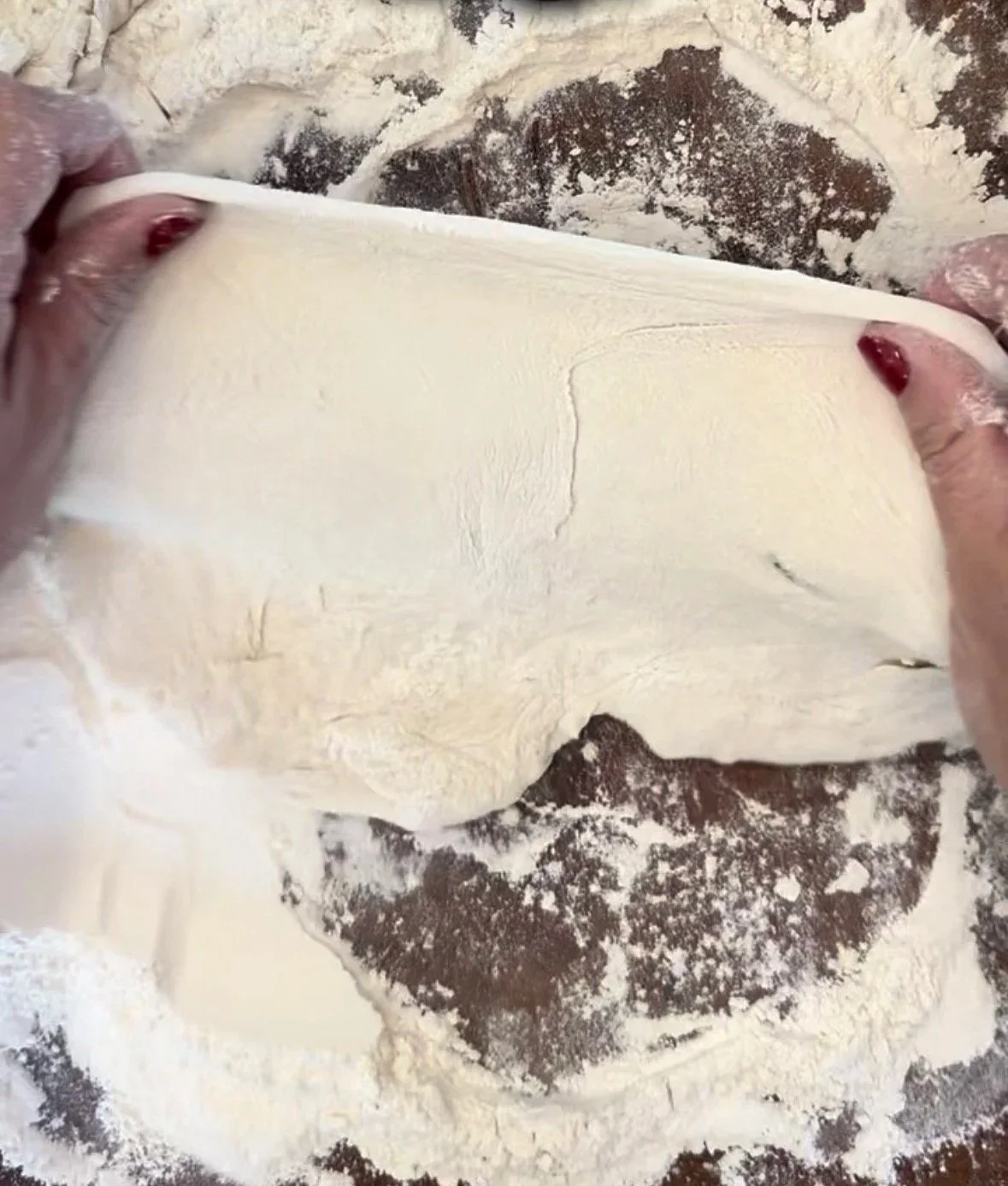 Hands kneading homemade pizza dough on a heavily floured wooden butcher block with a rolling pin nearby