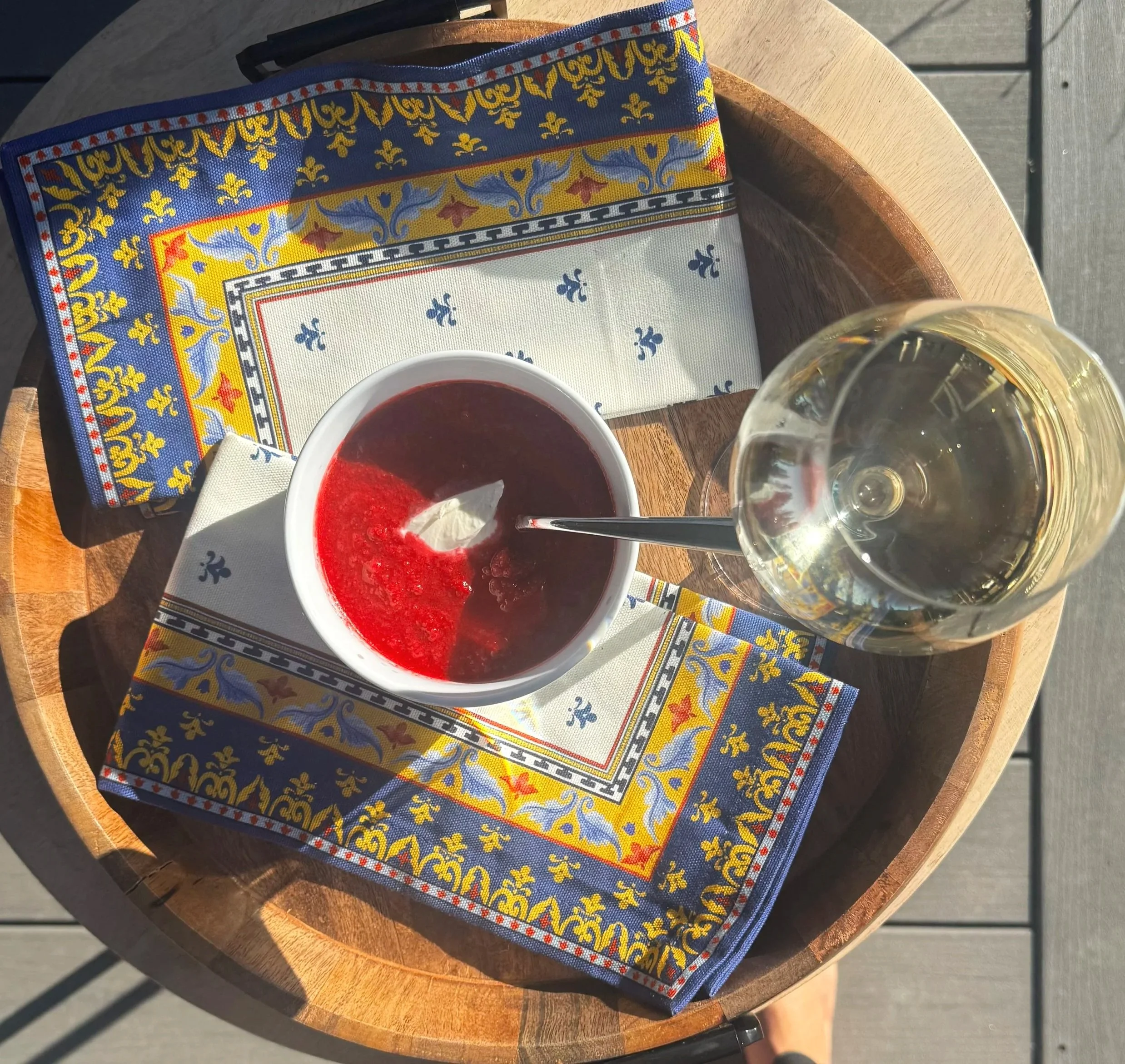 Gazpacho in bowl on napkins and wooden tray next to white wine in a glass