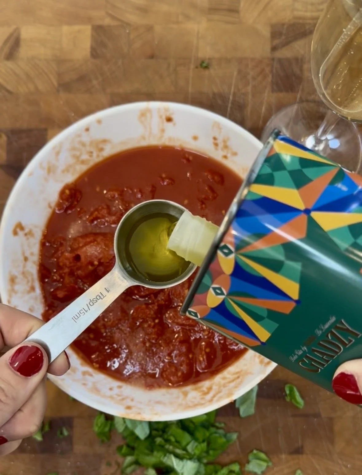 Pouring Giadzy organic extra virgin olive oil into a one tablespoon measuring spoon over a bowl of hand-crushed tomato pizza sauce