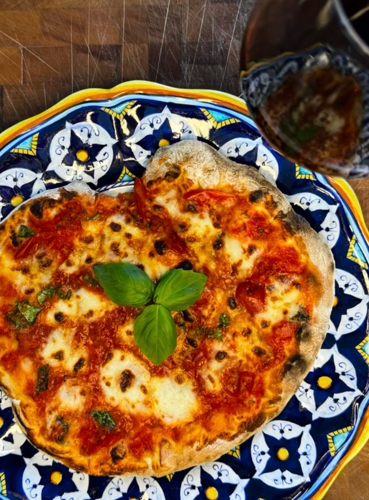 Wood fired homemade pizza margherita with charred crust and fresh basil on a blue and yellow Talavera ceramic plate on a butcher block surface