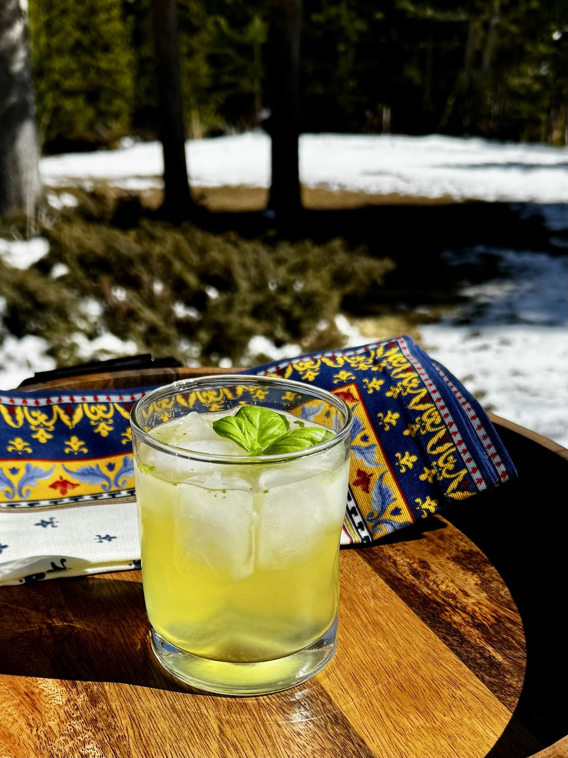 Almalfi Basil Smash cocktail on ice with basil garnish and limoncello on wood tray with napkin outdoors