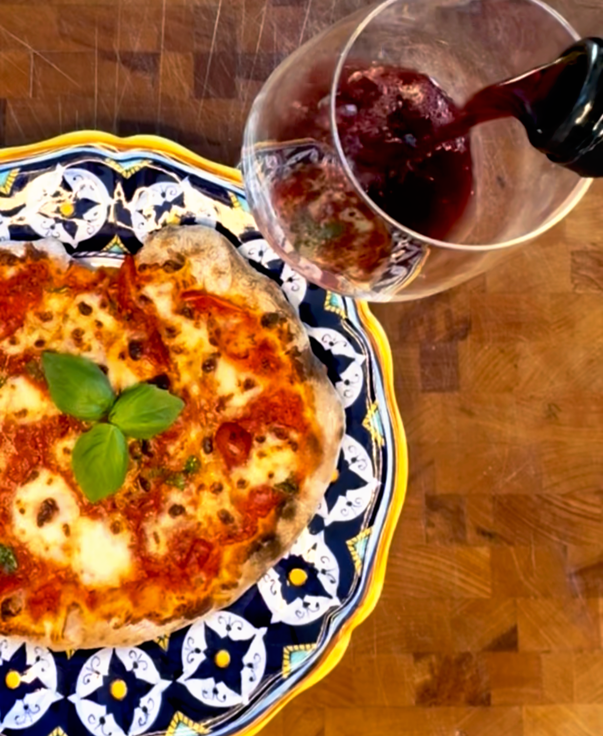 Pouring Francis Ford Coppola red wine into a glass next to a wood fired pizza on a blue Talavera plate on a butcher block — date night at home in Montana