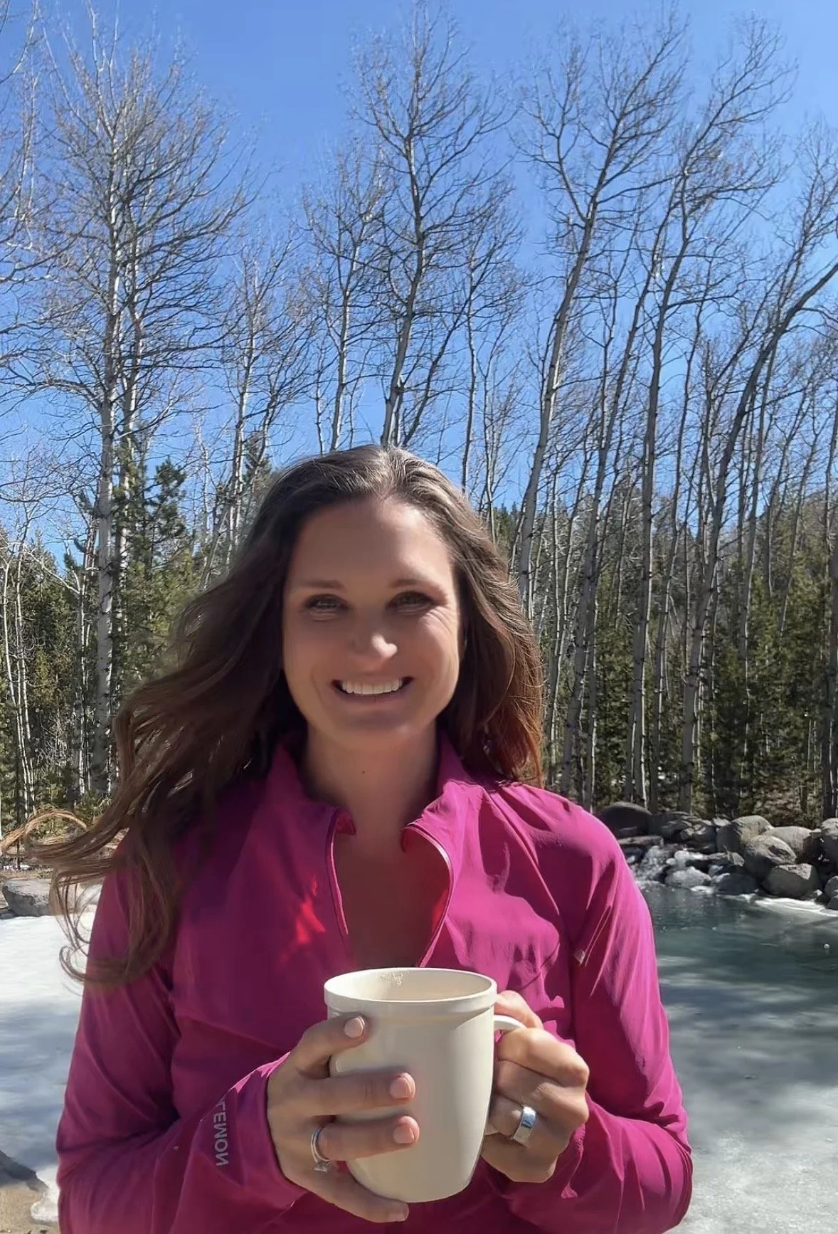 At Whiskey Ridge creator and blogger holding coffee mug and standing in front of a pond and aspen trees.