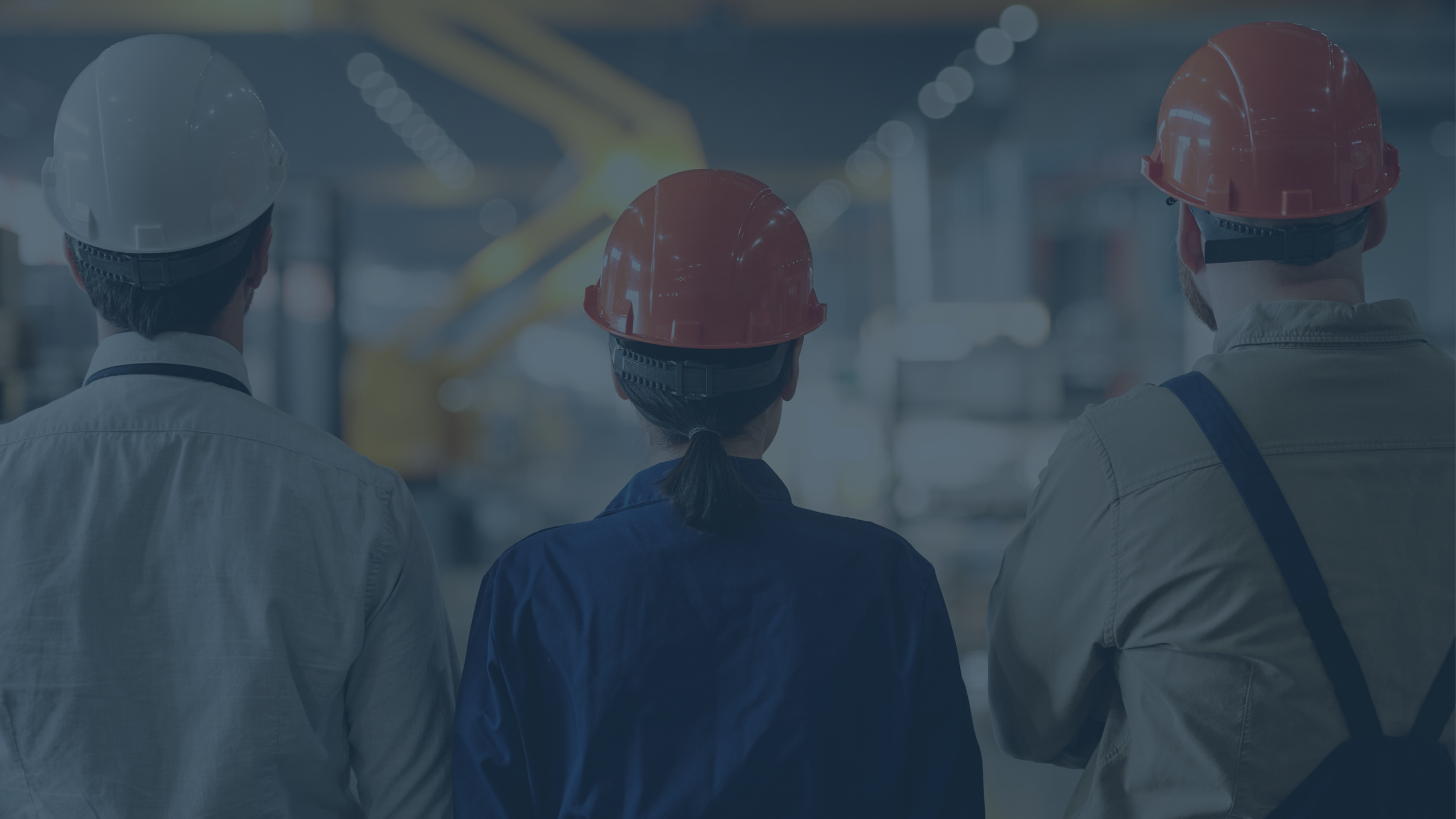 Three workers wearing safety helmets and work uniforms in an industrial setting.