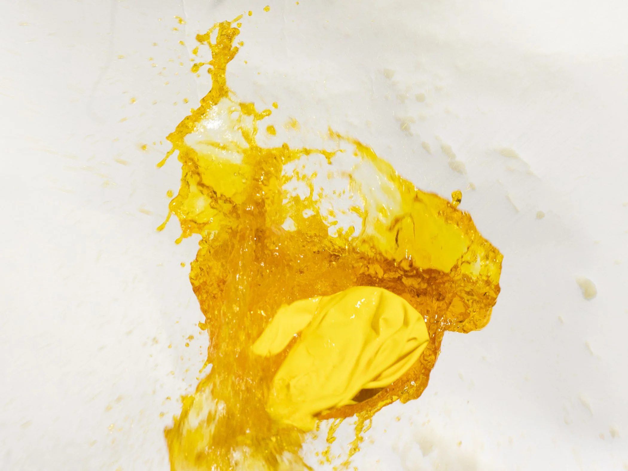 Yellow liquid splashing on a white surface, with a yellow object in the center.