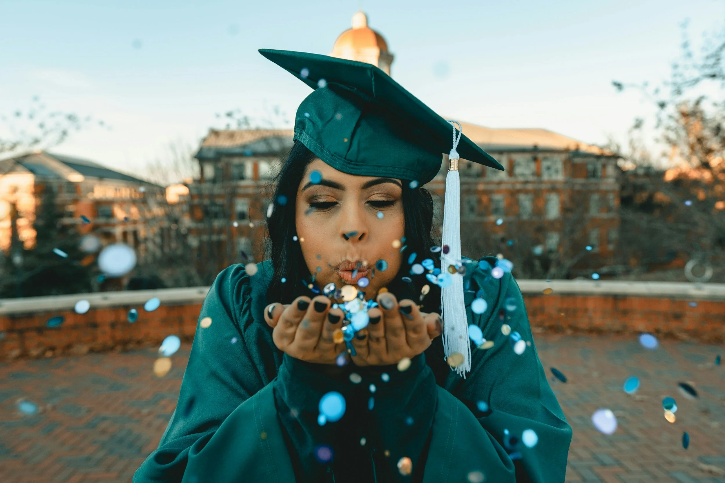 woman in a graduation cap and gown blowing confetti