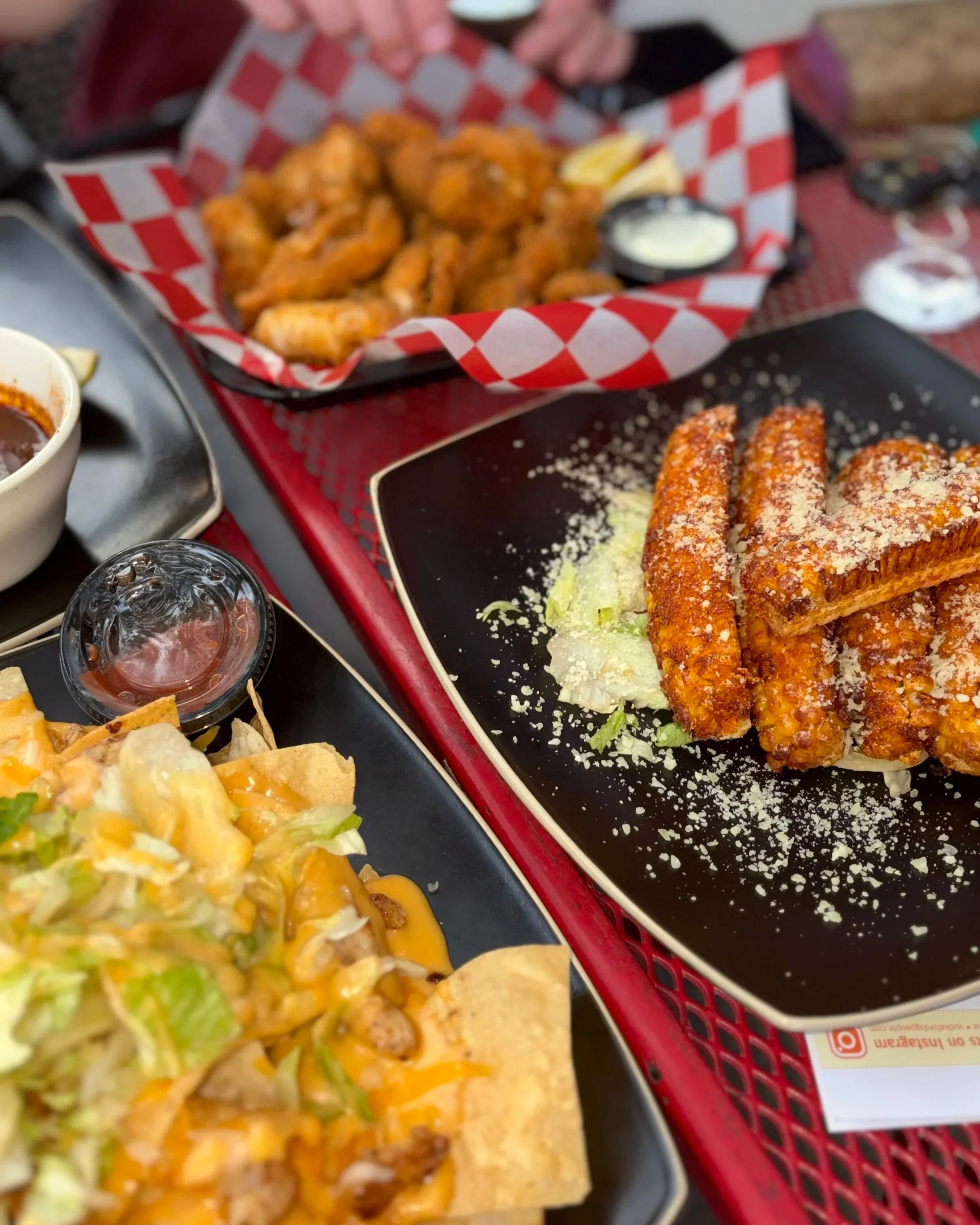 A shared table at 6ix Mears featuring seasoned corn ribs, loaded nachos, wings, and dipping sauces during Saturday Friends & Family Happy Hour.