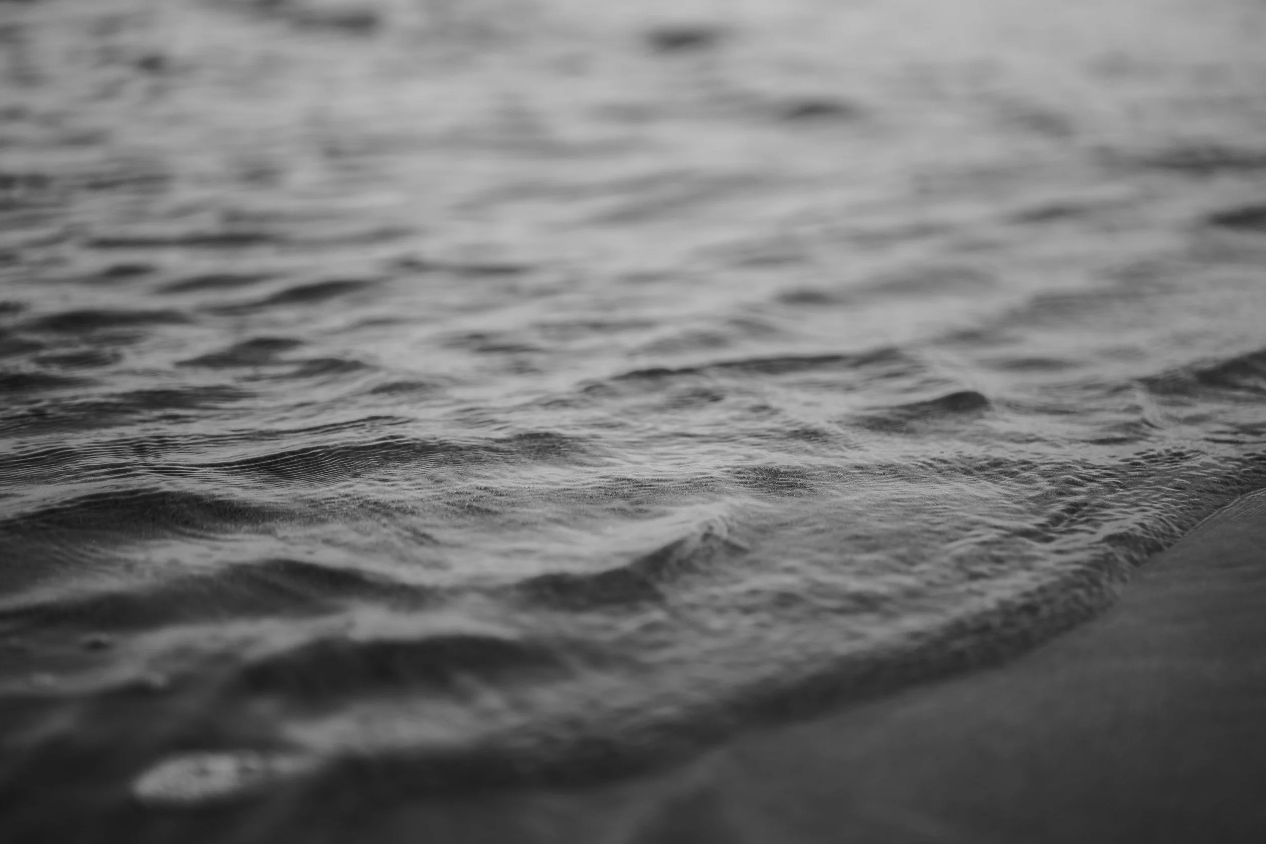 Close-up of calm ocean waves on a beach shoreline in black and white.