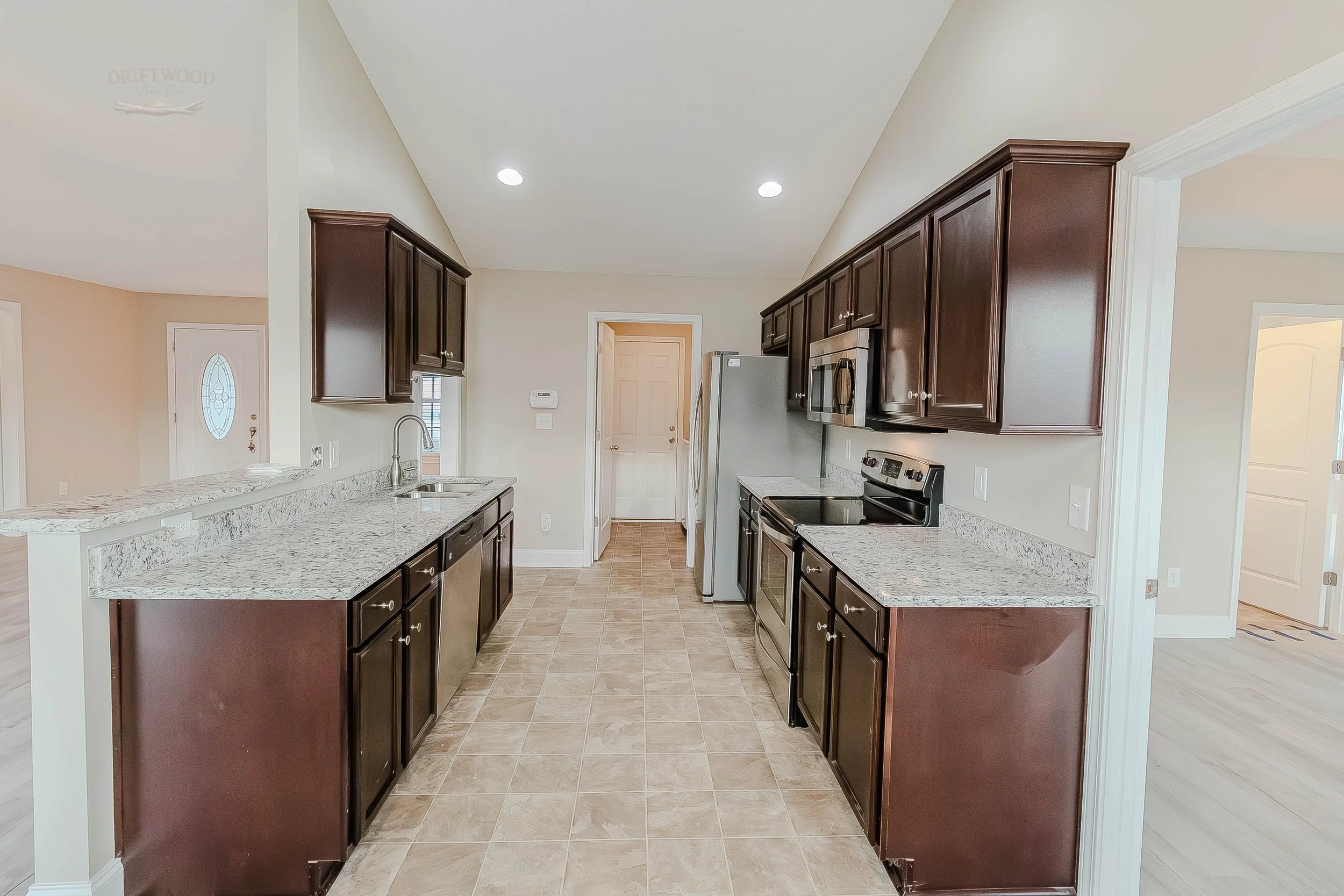 Kitchen with dark wood cabinets, granite countertops, stainless steel appliances, and beige tiled floor.