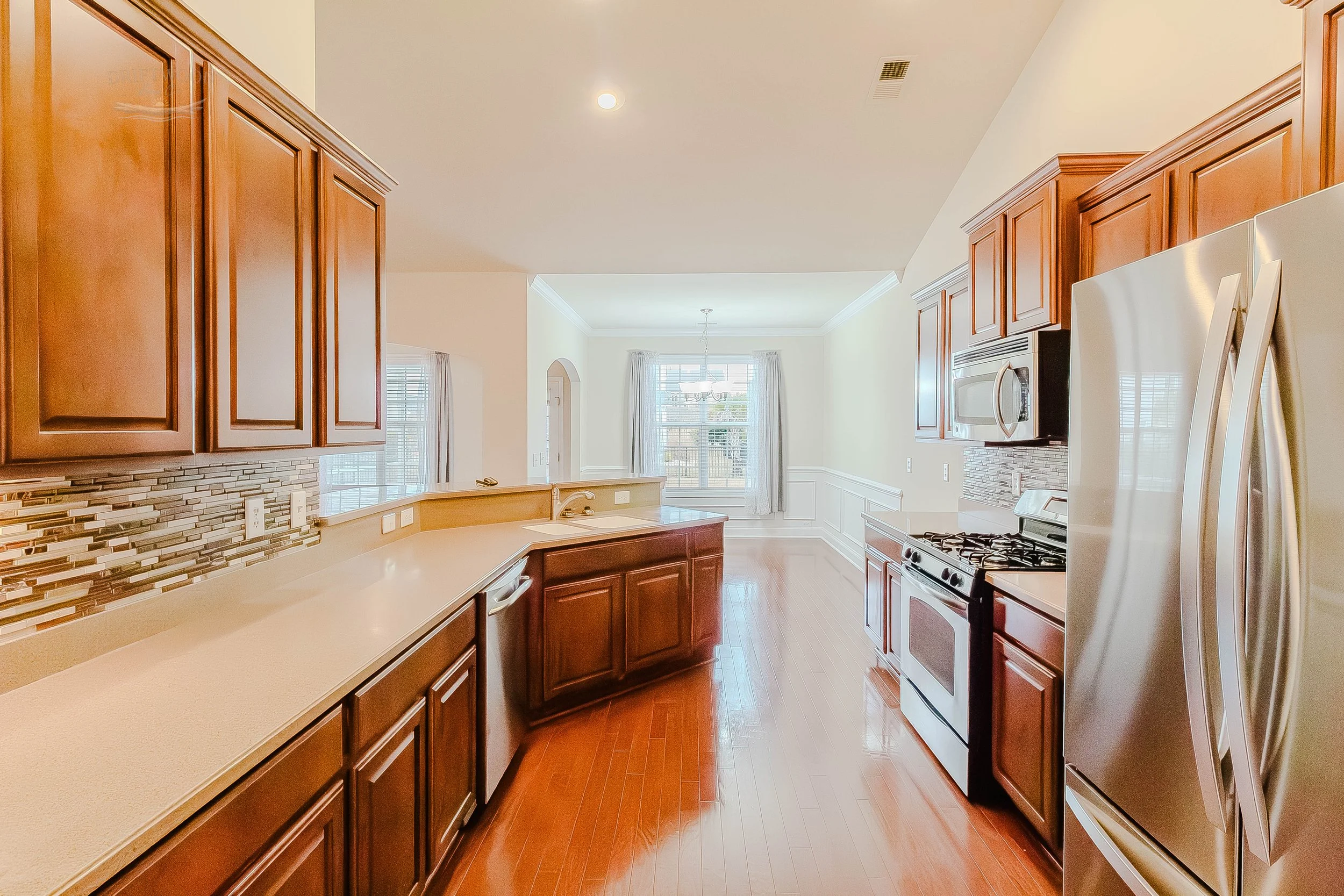 Bright kitchen with wooden cabinets, stainless steel appliances, and a dining area with a window and curtains.