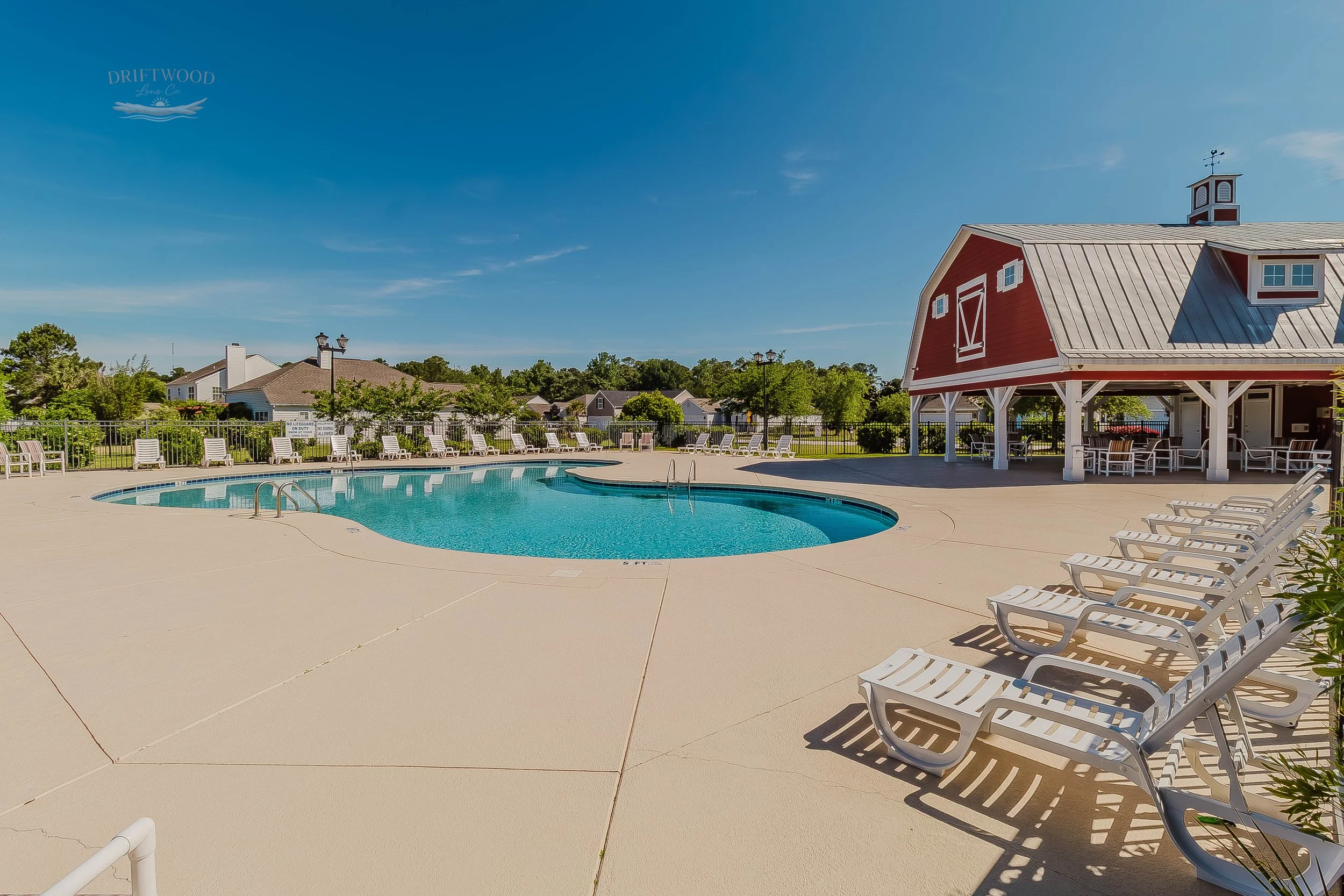Empty outdoor swimming pool with lounge chairs, a red barn-style building, and a clear blue sky.