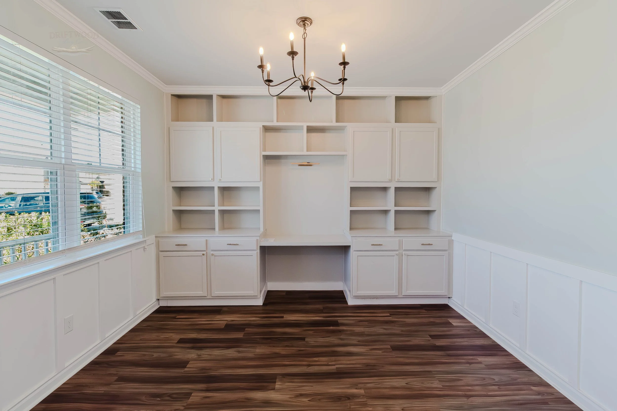 Empty room with built-in white cabinets, open shelving, wood flooring, a window with blinds, and a chandelier.