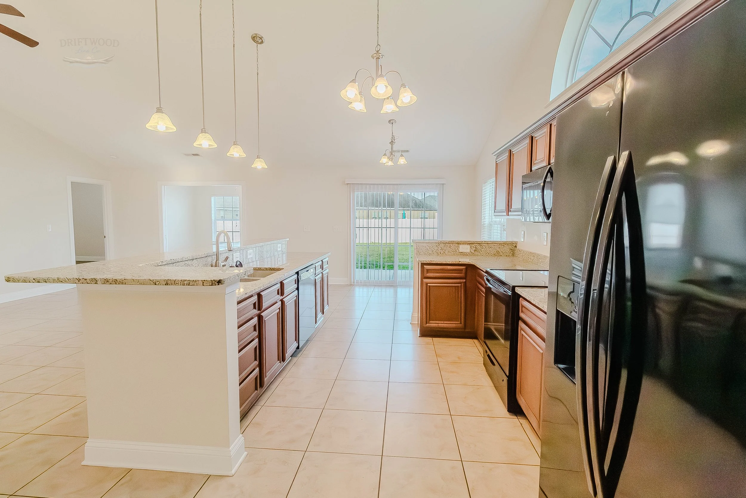 Empty kitchen with dark wood cabinets, black appliances, granite countertops, tiled floor, and a sliding glass door leading outside.