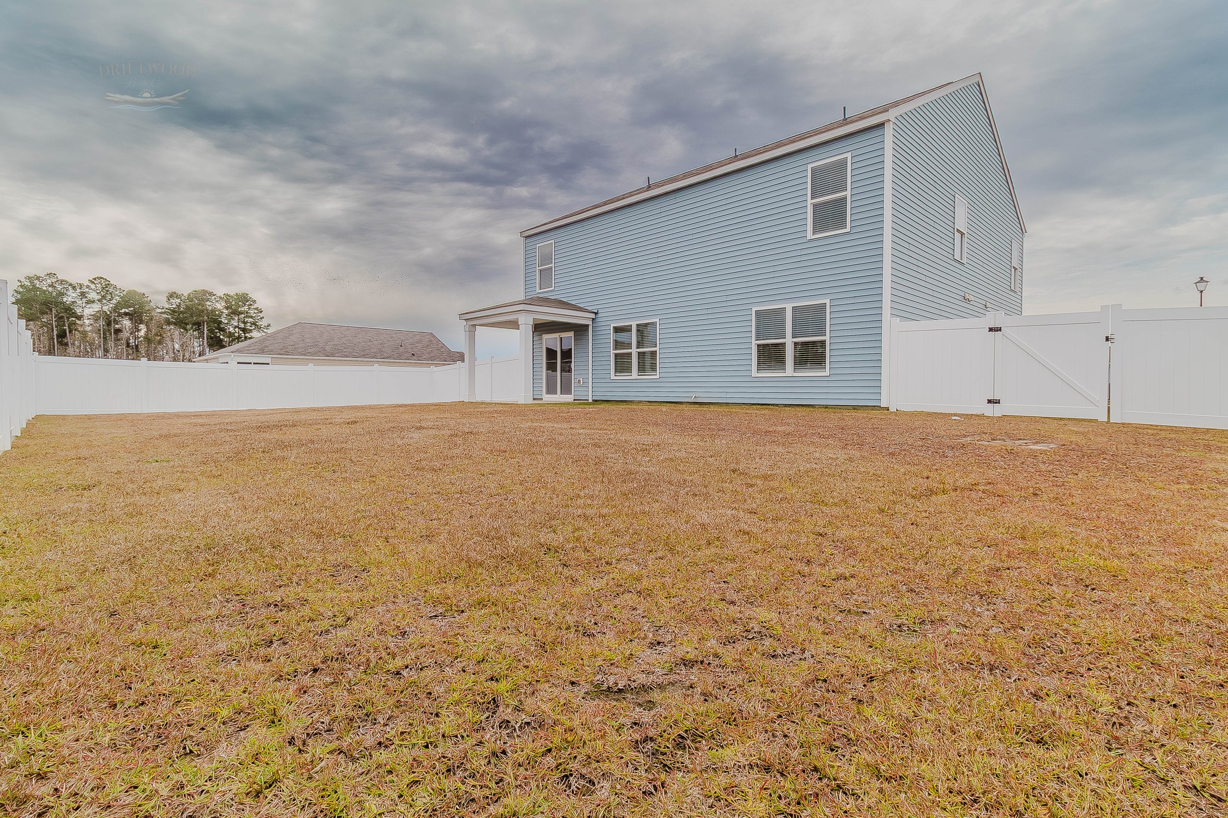 A blue two-story house with a fenced backyard and cloudy sky.