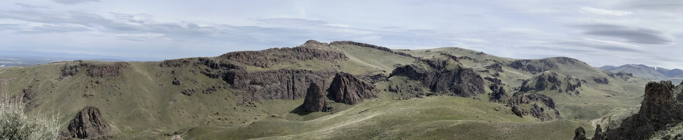 Panoramic view of green rolling hills with rugged rock formations under a cloudy sky.