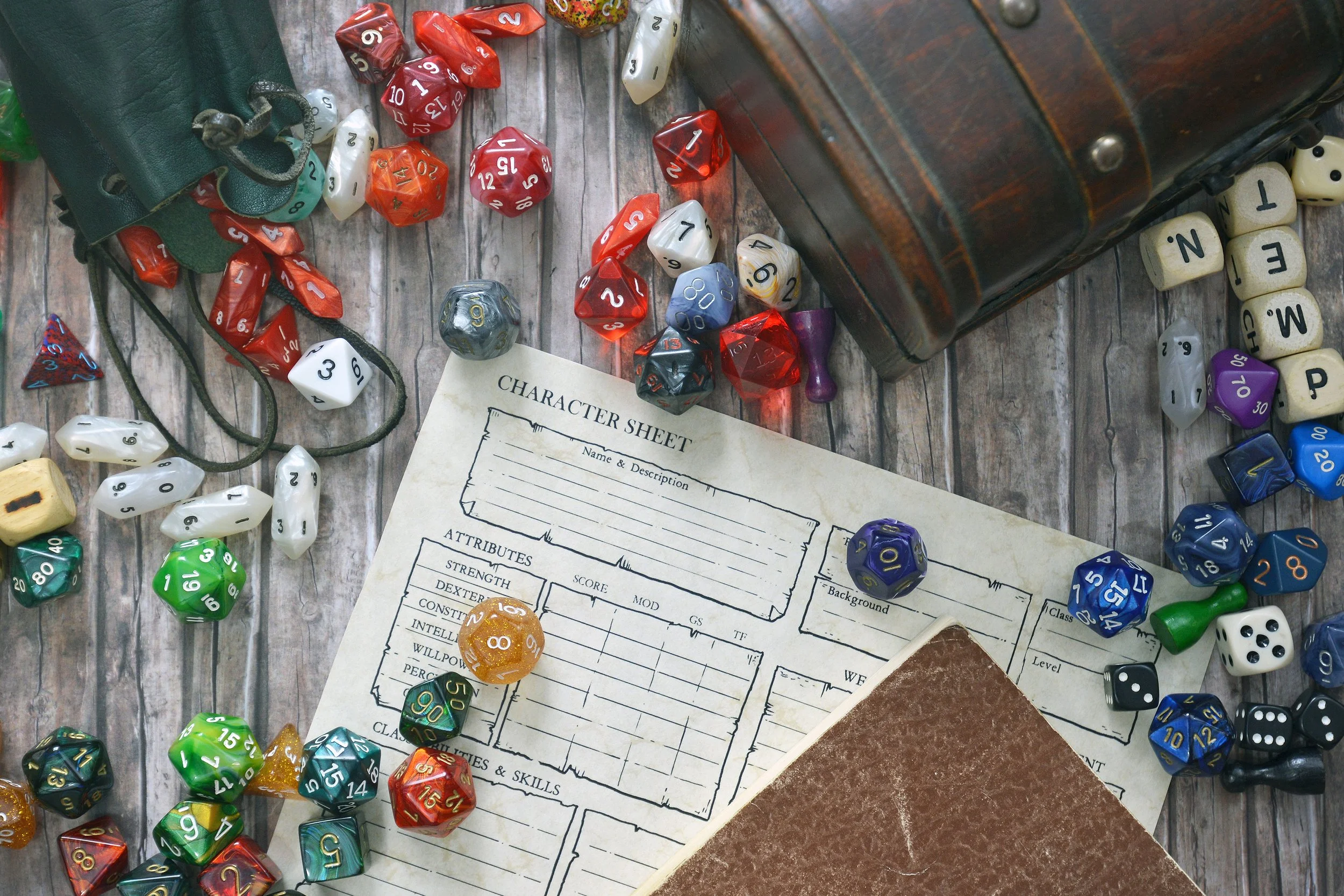 A table with a collection of multi-sided dice in various colors, a character sheet for tabletop role-playing games, and a small wooden chest, suggesting a gaming setup.