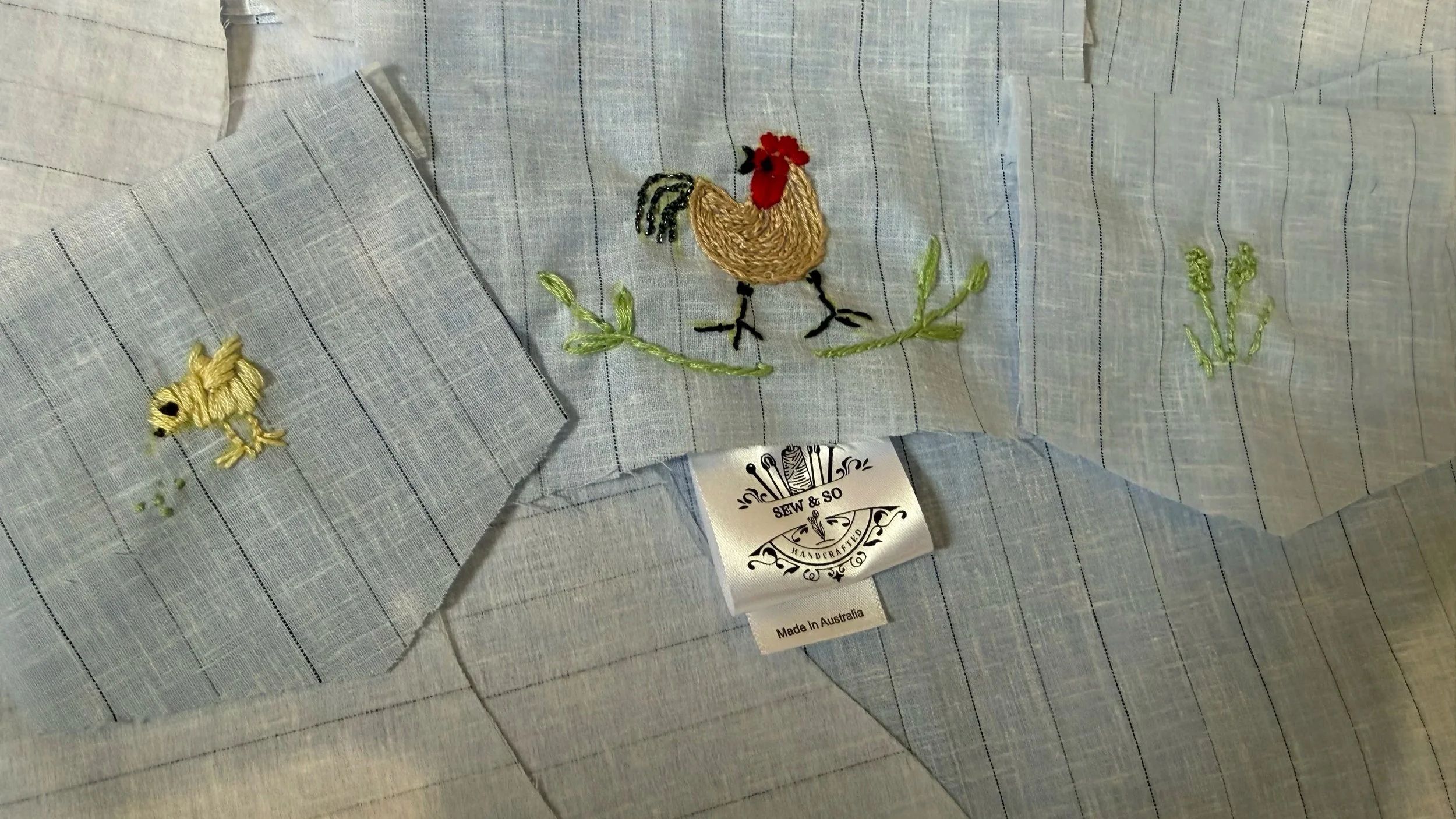 Light blue embroidered fabric with two patches, one of a small yellow chick and another of a brown hen with a red comb, black legs, and green grass embroidery. A black and white label reads "SEW & SO HANDCRAFTED" and "Made in Australia".