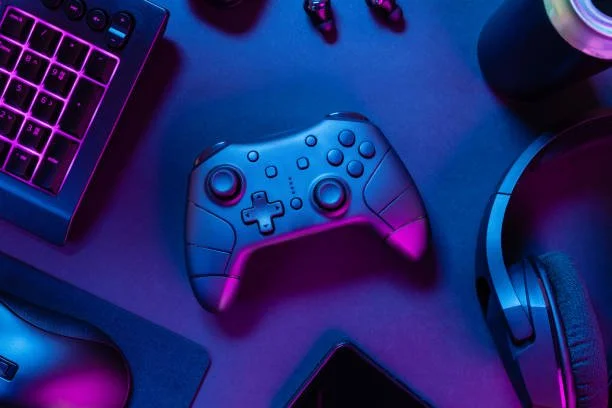 Gaming setup with a keyboard, game controller, headphones, and a drink on a desk illuminated with purple and blue lighting.