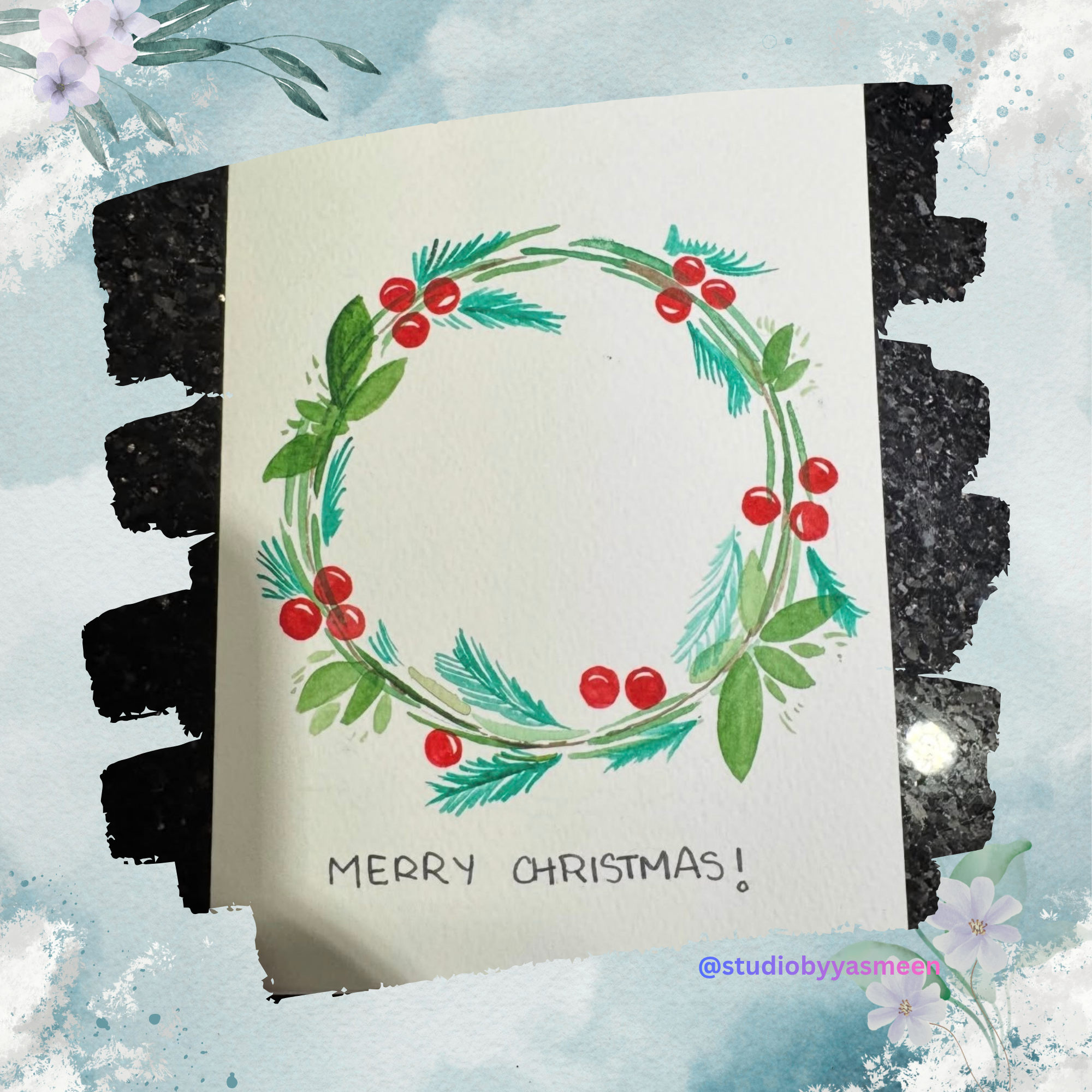 A Christmas card with a painted wreath of green leaves, red berries, and blue pine needles, with the message 'Merry Christmas!' written below. The card is surrounded by a decorative frame with flowers and watercolor effects.