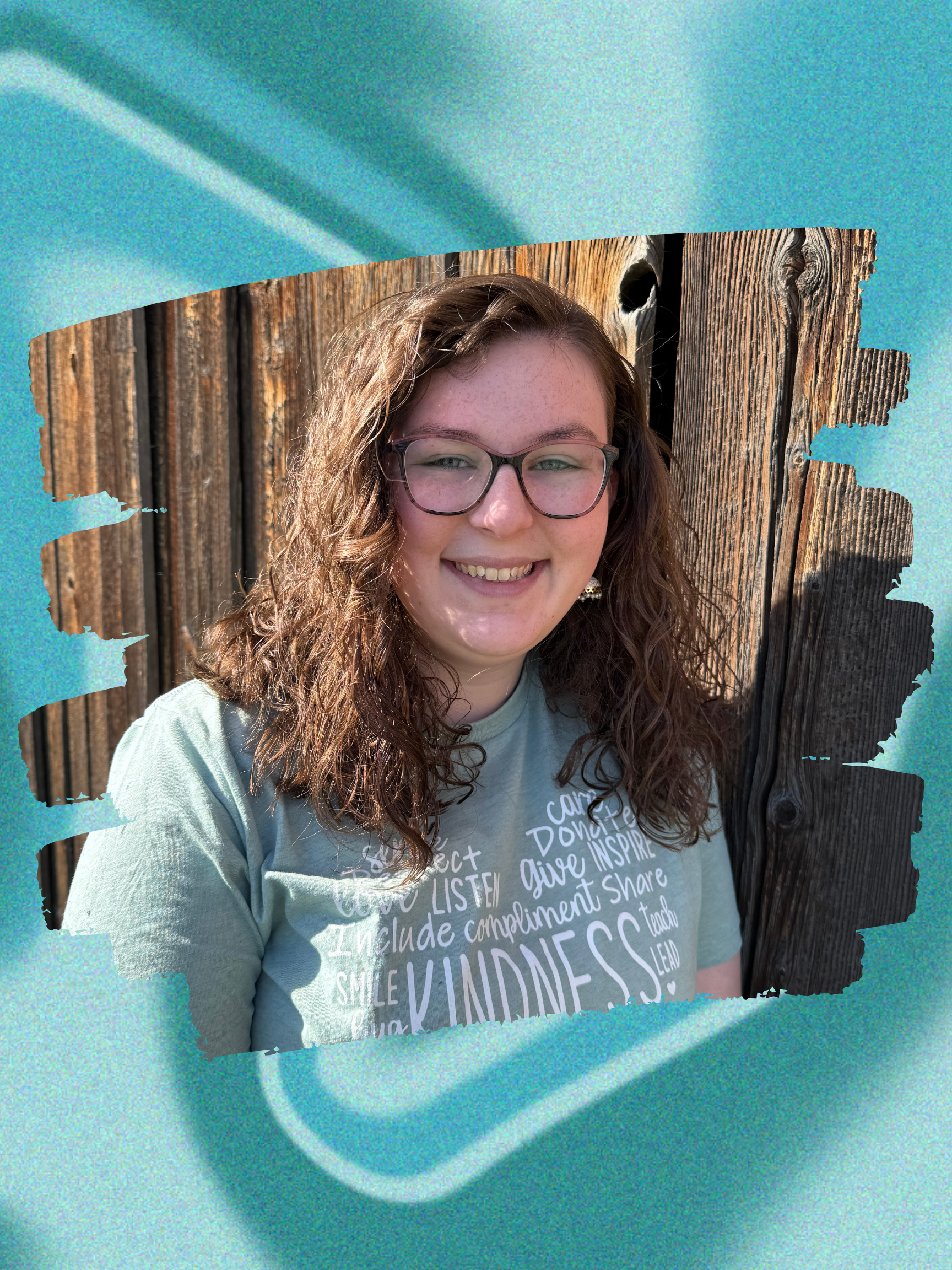 Photograph of a young woman with curly brown hair and glasses, smiling, standing in front of a wooden fence, framed by a torn paper effect on a textured blue background.