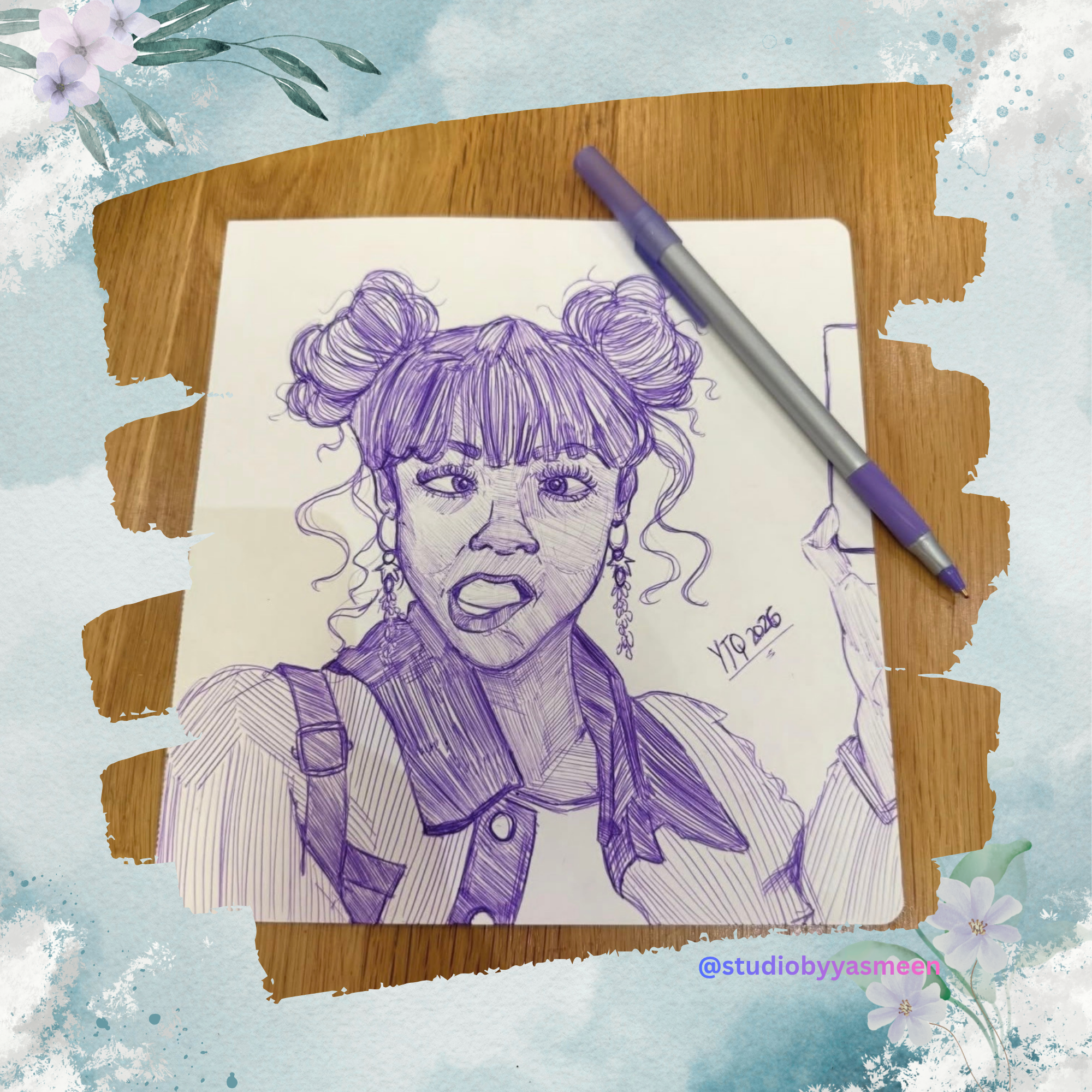 A purple ink sketch of a young woman with double buns hairstyle, earrings, and a surprised expression holding a phone, on a white paper with a wooden surface nearby, and a pen resting on the paper. The paper has a signature 'Y10 2026' and '@studiobyyasmeen' is written at the bottom right corner.