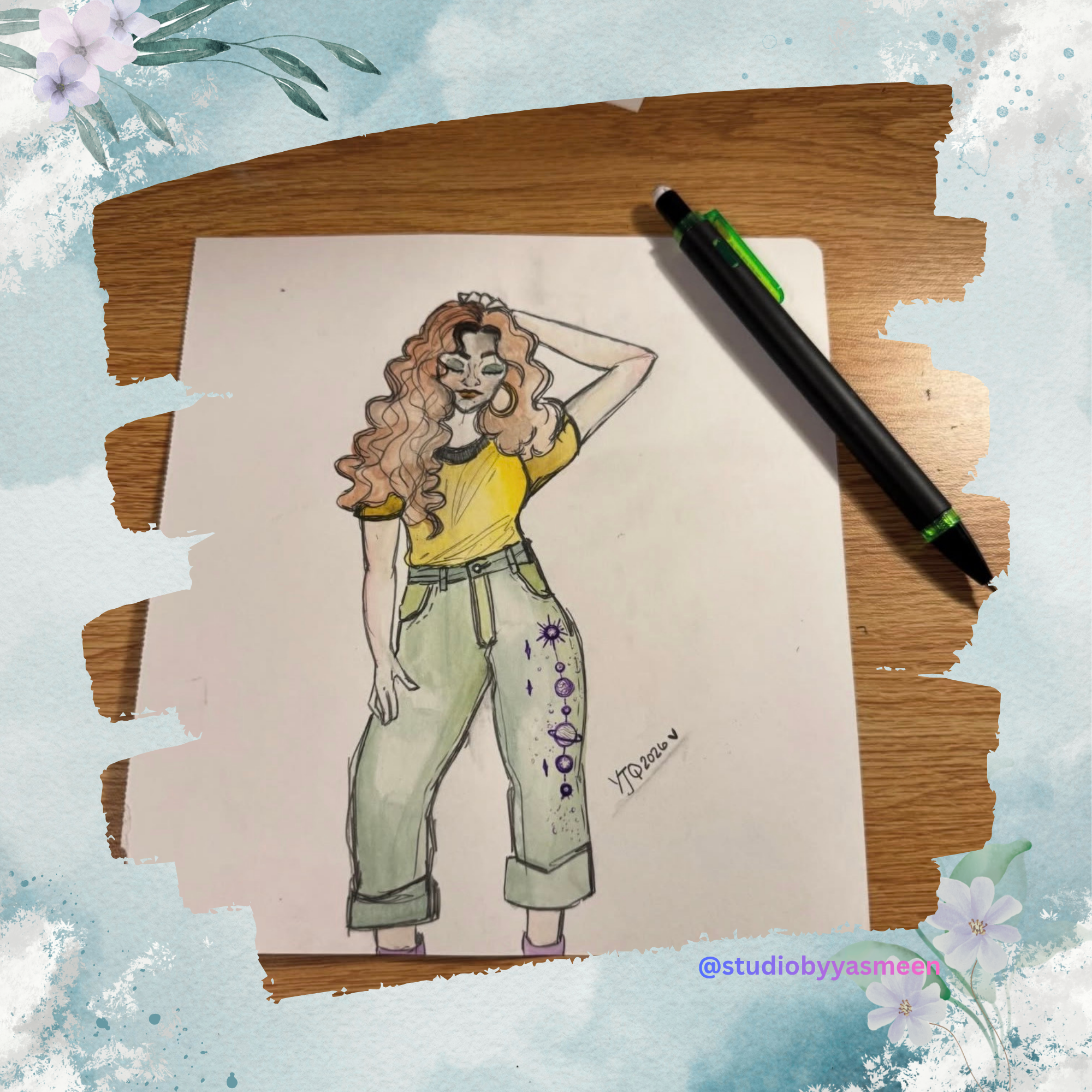 A hand-drawn fashion illustration of a woman with curly hair, wearing a yellow T-shirt and light green high-waisted jeans with celestial and planetary designs on one leg, is placed on a wooden surface with a black marker pen beside it. The illustration is signed 'YJ 2020' and is surrounded by a decorative floral and watercolor border.