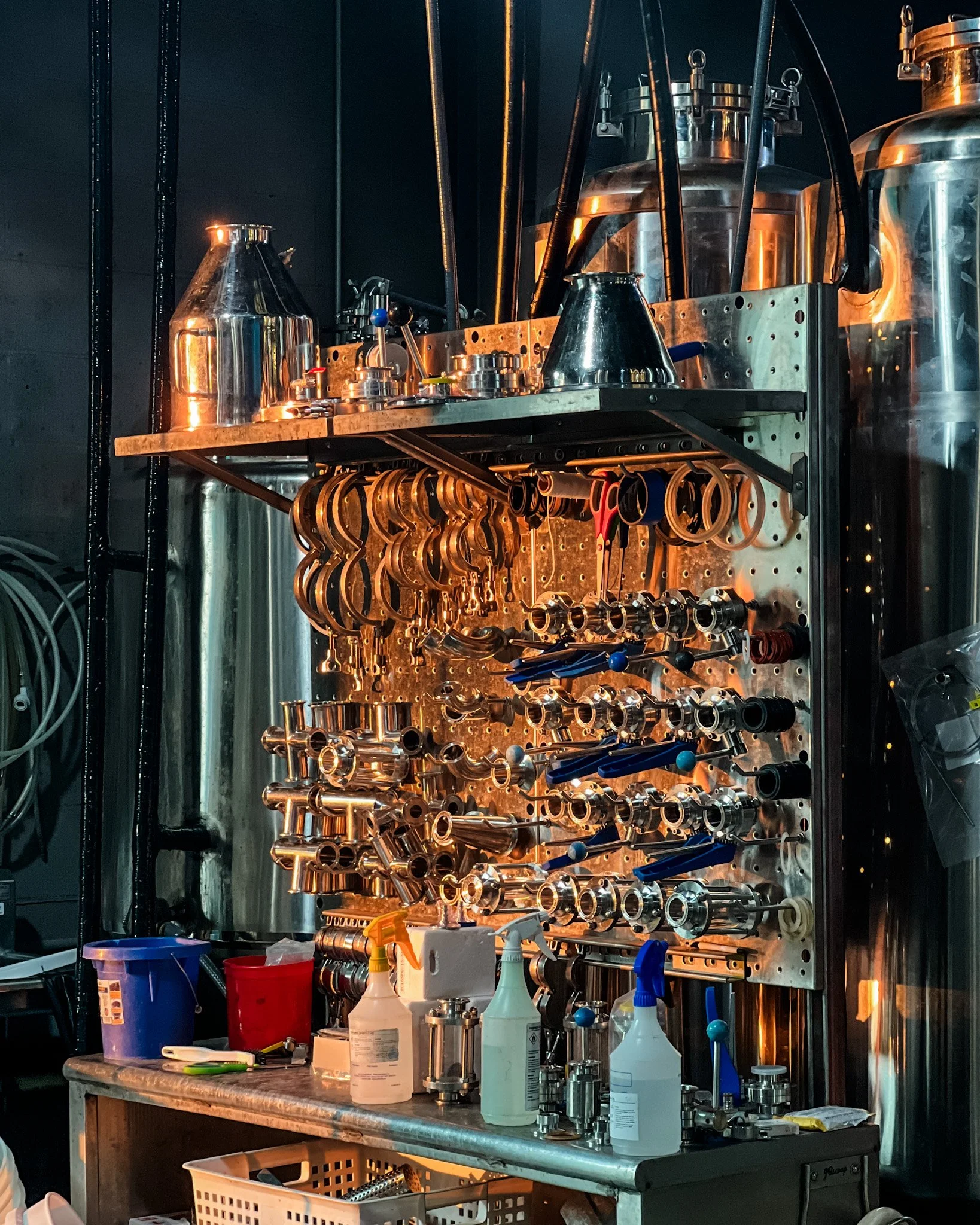 Laboratory workbench with metal pipes, tools, and cleaning supplies, set against a dark wall with equipment rack.